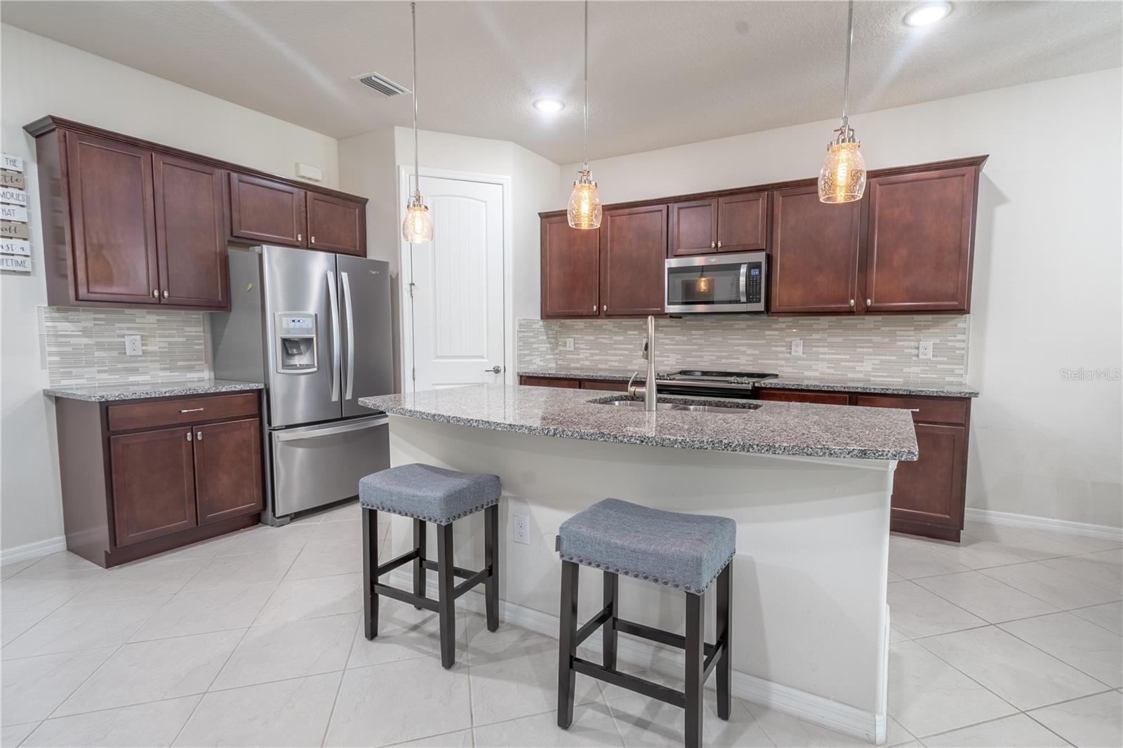 The kitchen features a large island with a breakfast bar, granite countertop, a stainless steel sink with a touchless faucet, and a dishwasher.