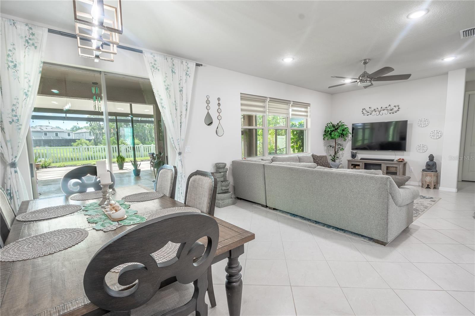 The dining room features a striking chandelier, ceramic tile flooring, neutral tones and sliding glass doors that open to the 25' x 40' Lanai