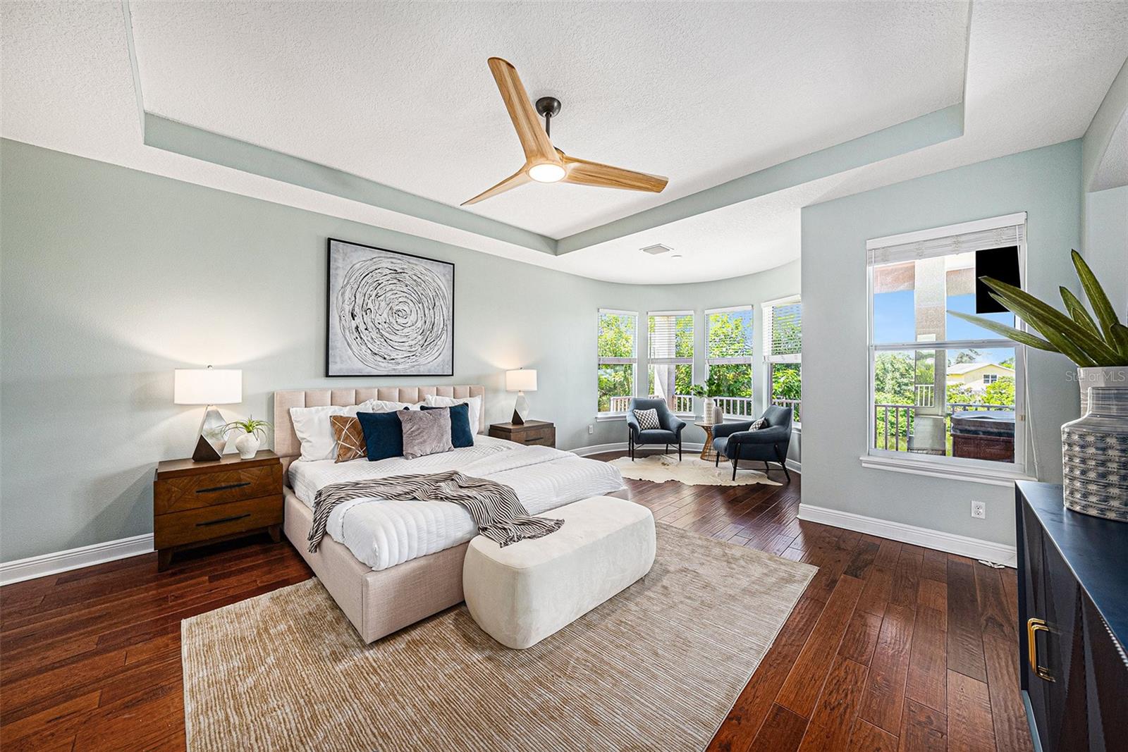 Primary bedroom with tray ceiling and separate sitting area overlooking the water