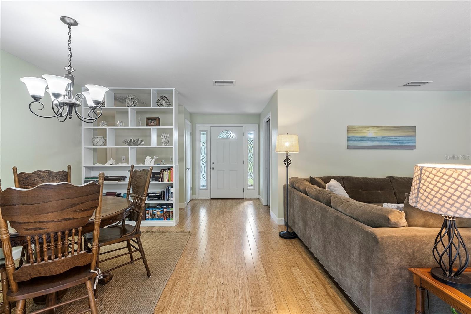 View of front door from the back of the living room.  To the right of the front door is the kitchen. Behind the built-in bookcase and shelves is a hallway to the guest wing