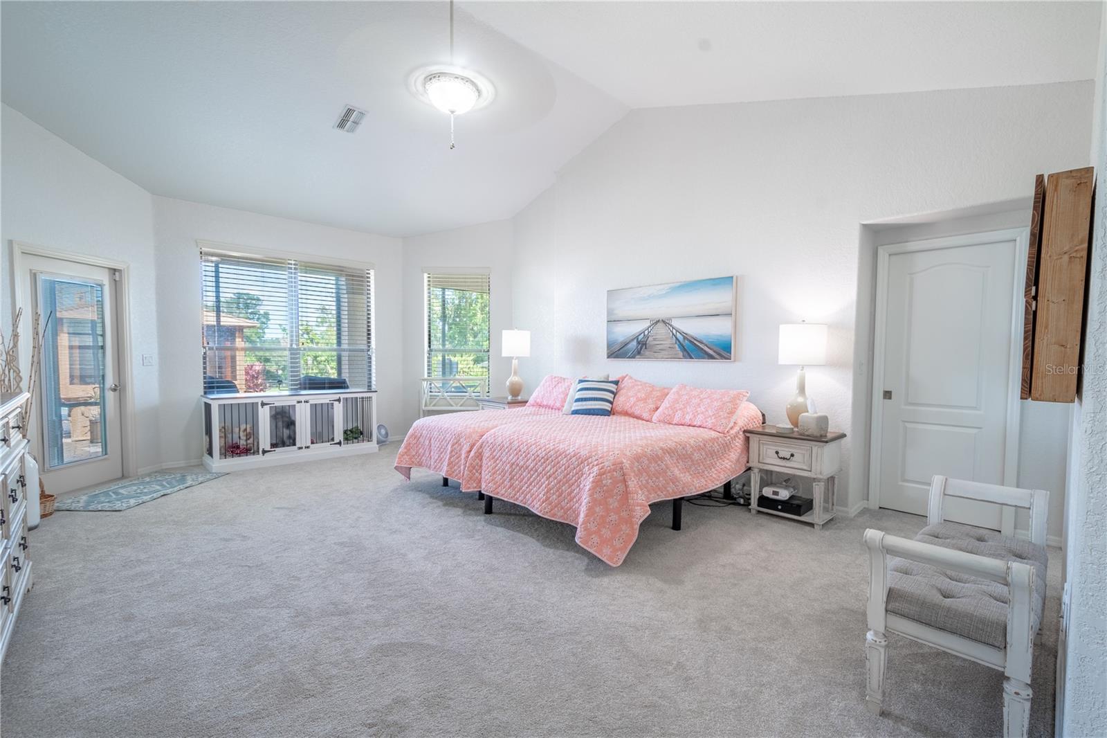 The Primary bedroom features neutral tones, plush carpet, a walk-in closet, a vaulted ceiling with ceiling fan, a French door to the lanai and an ensuite bath.