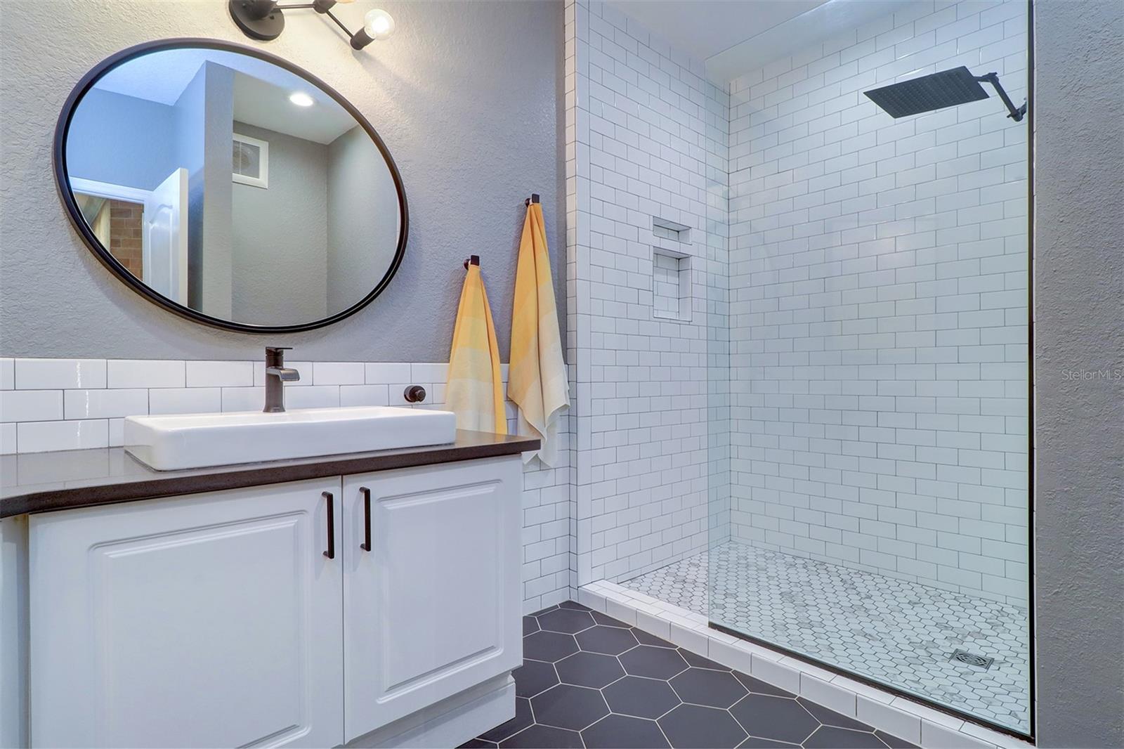 Deluxe primary bath  white subway tile shower with hexagon tile flooring and glass panel shower door