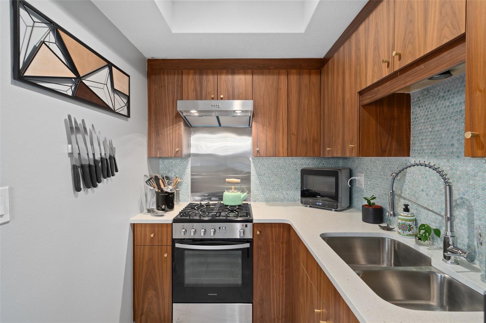 The kitchen features a gas range and oven with exhaust fan, stone counters and a double basin stainless steel sink.