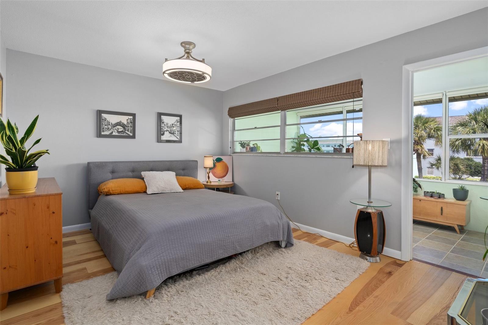 The primary bedroom features neutral tones, engineered hardwood floor and a modern, decorative ceiling fan and light.