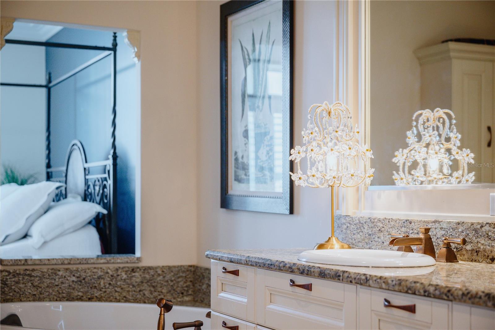 Elegant details in the en suite bath create a serene and luxurious atmosphere, with ornate lighting and a glimpse into the inviting primary bedroom.