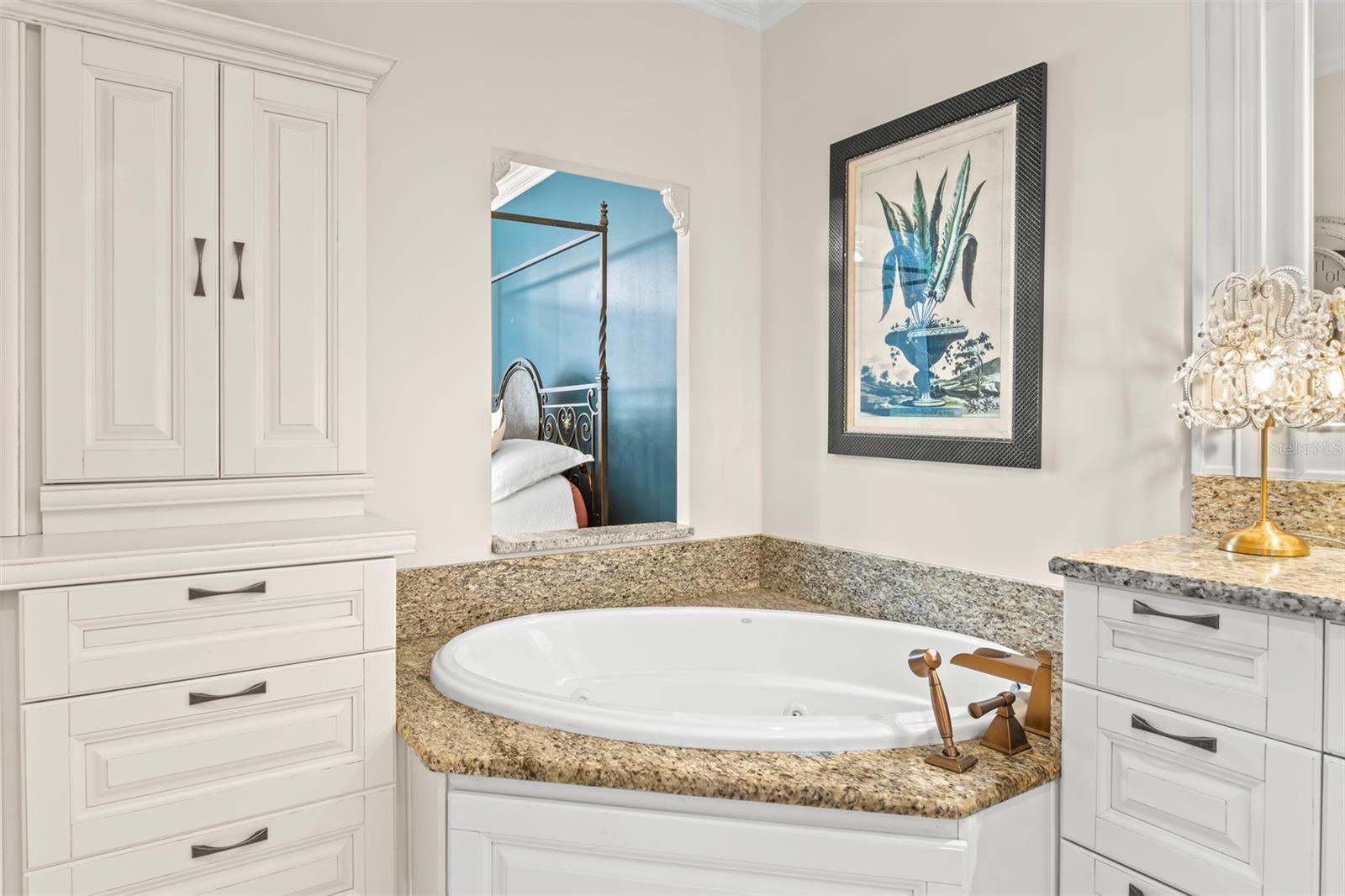 Relax and unwind in the luxurious jetted tub, perfectly complemented by elegant cabinetry and a peek into the cozy primary bedroom.