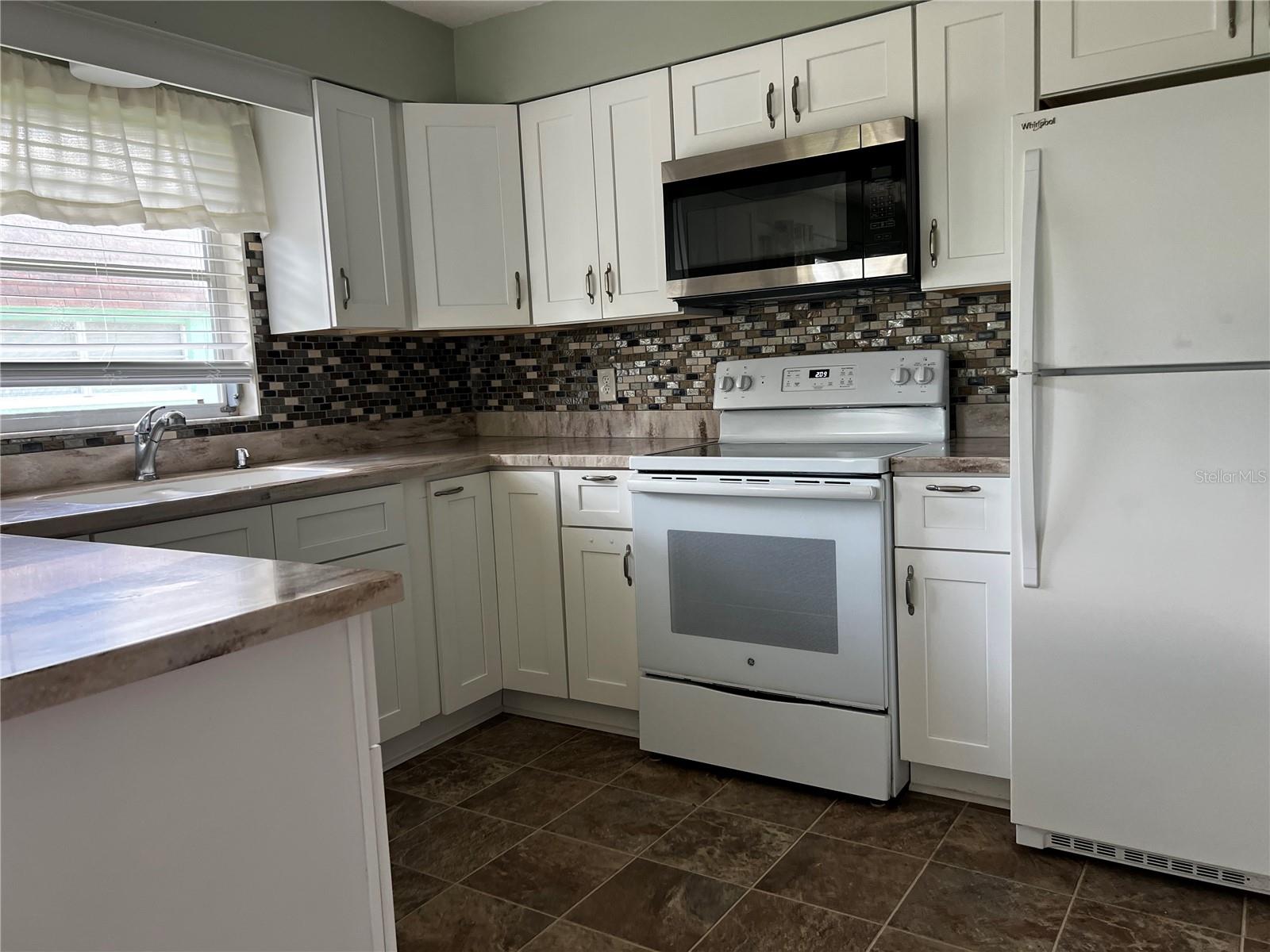 Kitchen with solid counters, range and refrigerator/freezer with ice maker.