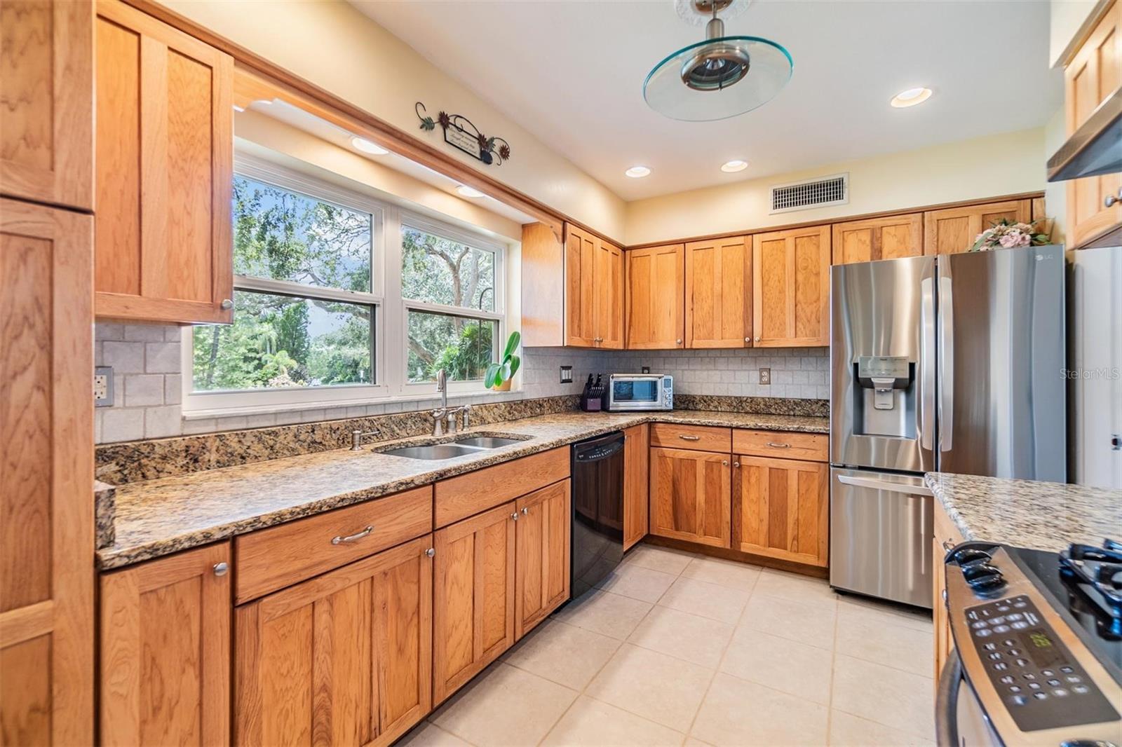 Kitchen with ample storage and counter space, gas stove, stainless steel refrigerator, and double windows overlooking front landscaping and circular driveway.