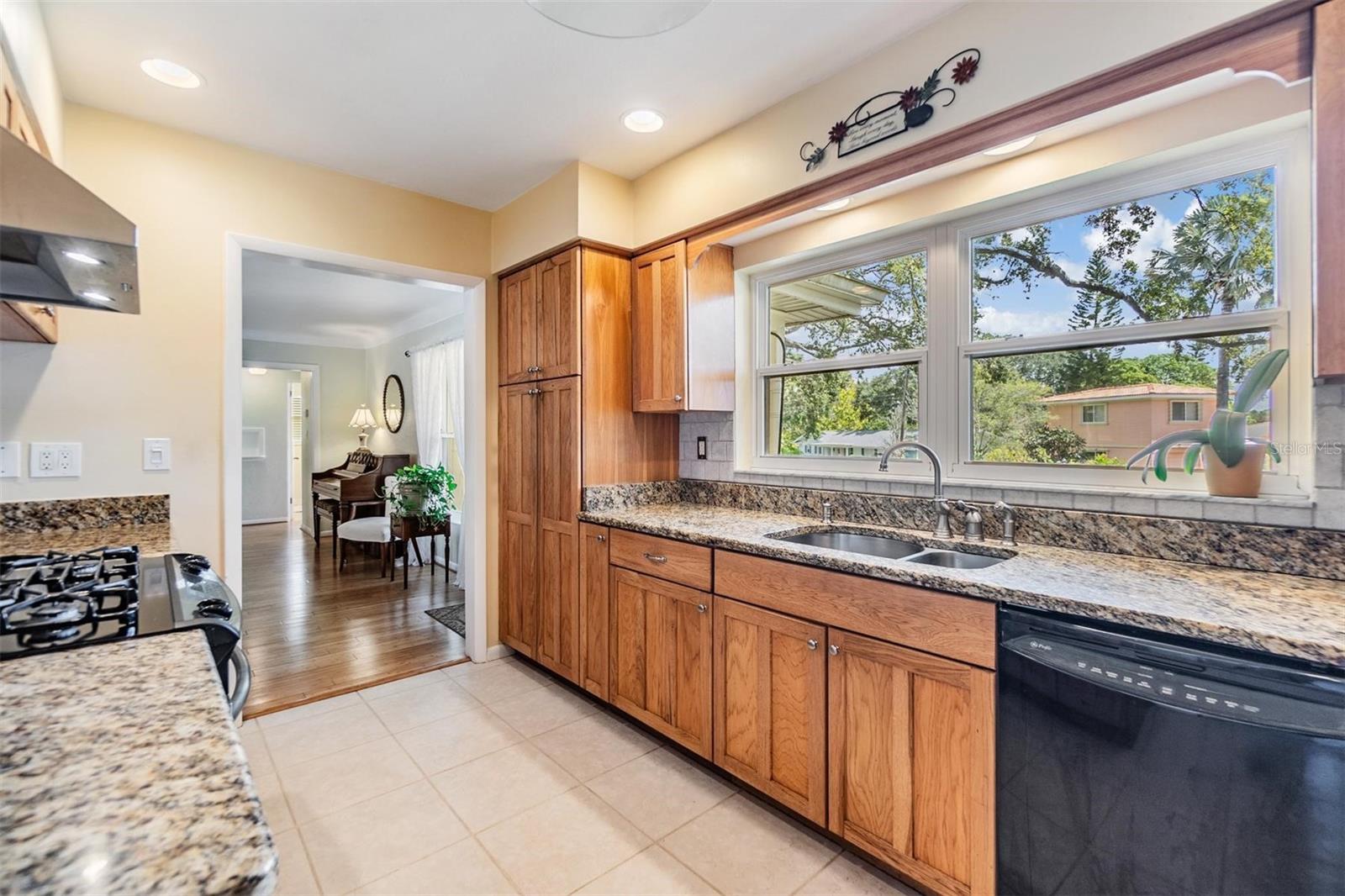 Kitchen with ample storage and counter space, gas stove, stainless steel refrigerator, and double windows overlooking front landscaping and circular driveway