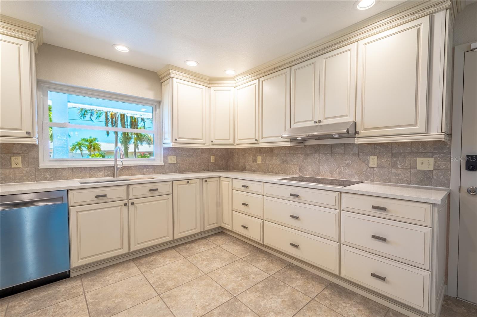 The stainless steel sink sits beneath a window with a tropical view.