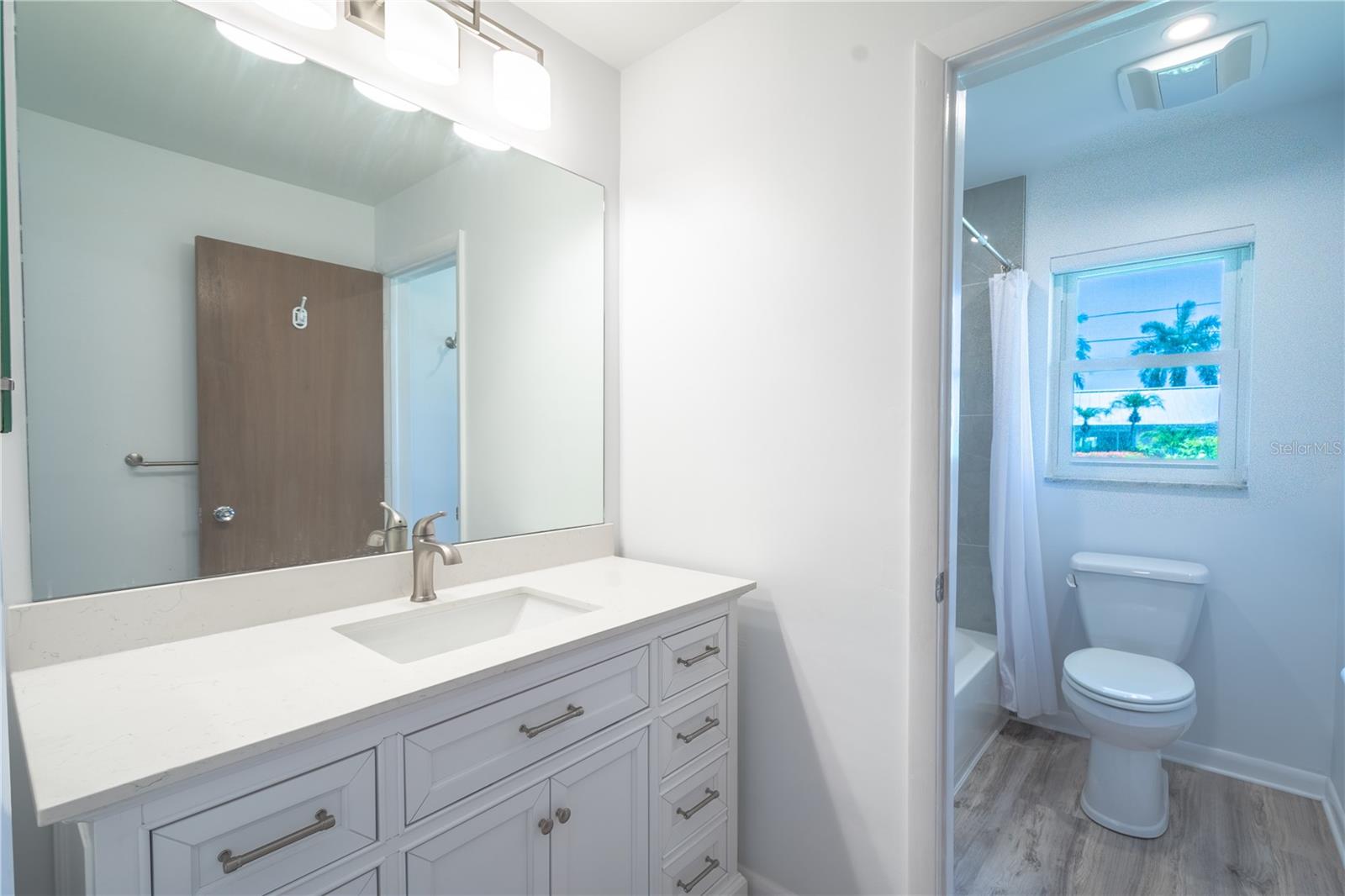 The 2nd bathroom features a mirrored vanity with quartz countertop, storage and a downlight fixture.