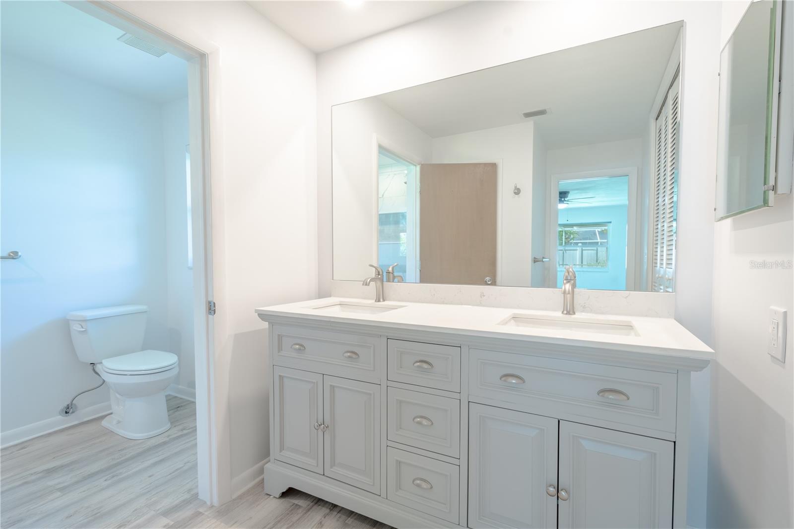 The primary bathroom features a private water closet and a mirrored vanity with dual sinks and storage, a quartz countertop and recessed lighting.