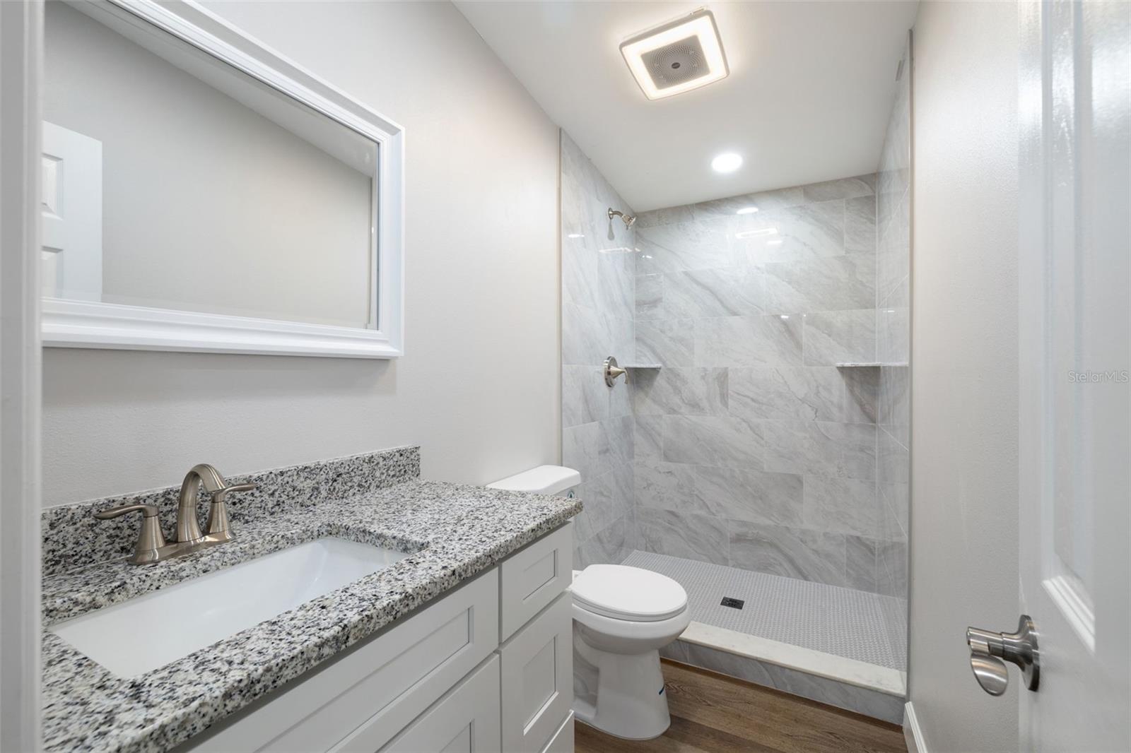 Secondary Bathroom with new granite topped vanity with soft-close drawers, comfort height toilet, recessed lighting, fixtures, flooring, a custom tiled walk in shower AND another SMART HOME fan with ambient lighting!  Play music from your phone...change colors!  Its amazing!