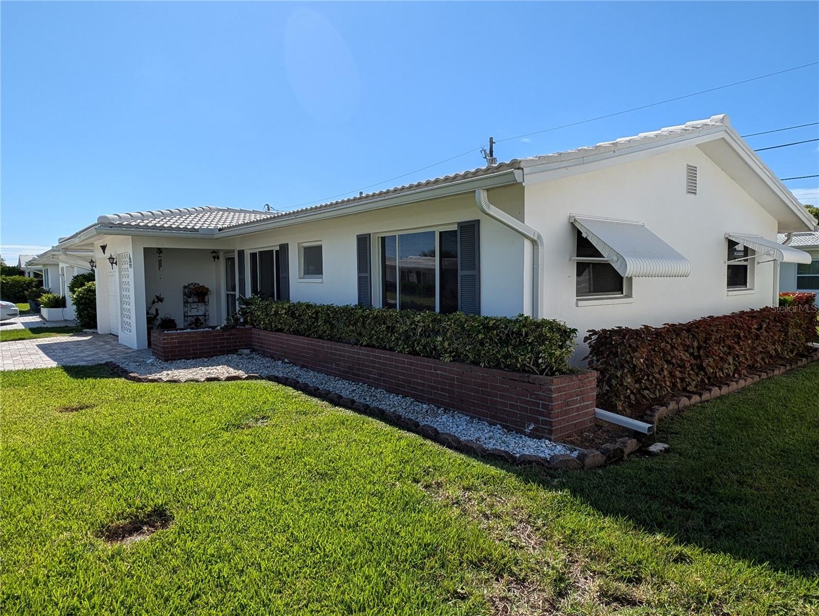 Front and side exterior view.  Exterior features include: pavered driveway & entry (2020), gutters/downspouts, updated windows, drop down awnings, tile roof (2023) and nicely manicured landscaping.