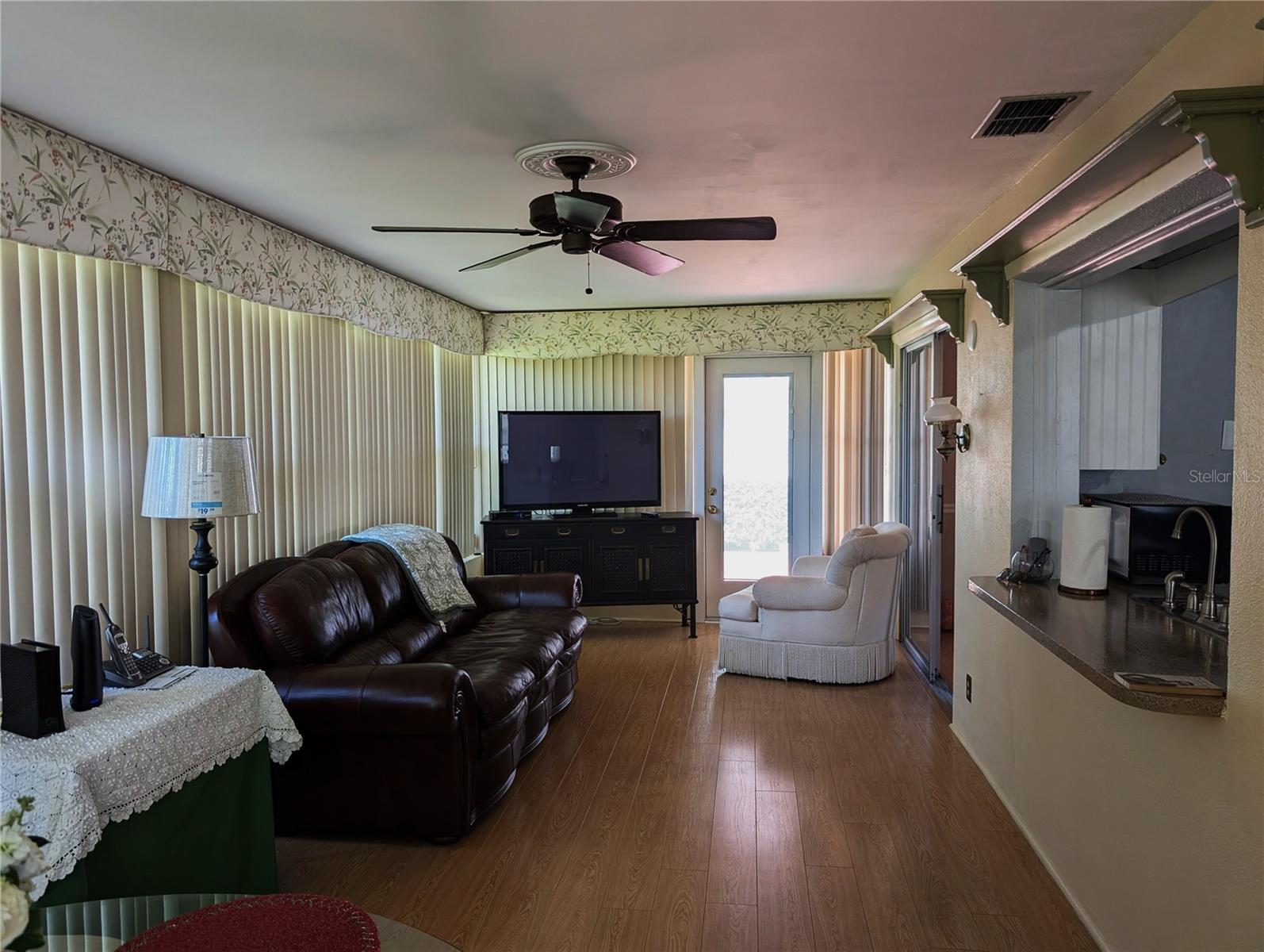 View thru Florida room to new back door entry.  Pass thru window to kitchen on right.  Wall of windows provides an abundance of natural light.  Ceiling fan is mounted on a decorative medallion.