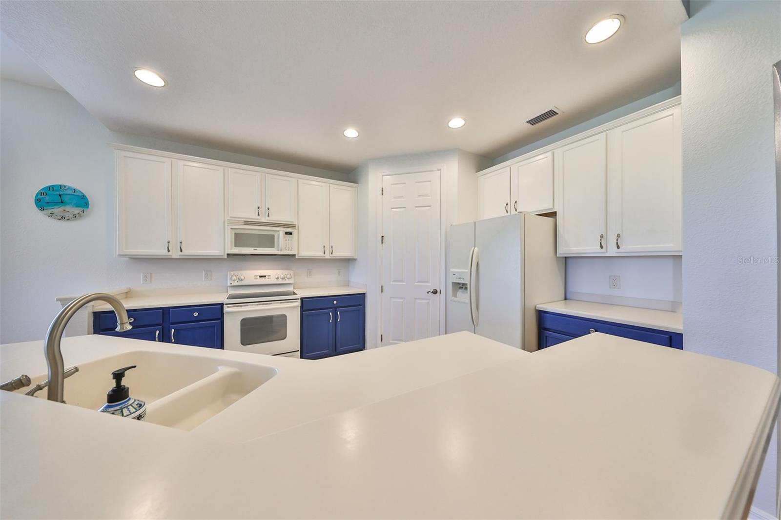 The Kitchen Countertops are neutral and clean Corian cabinets. Notice the recessed lighting and undercounter lights, in addition to the natural light that flows through the kitchen. Lots of room for multiple cooks.