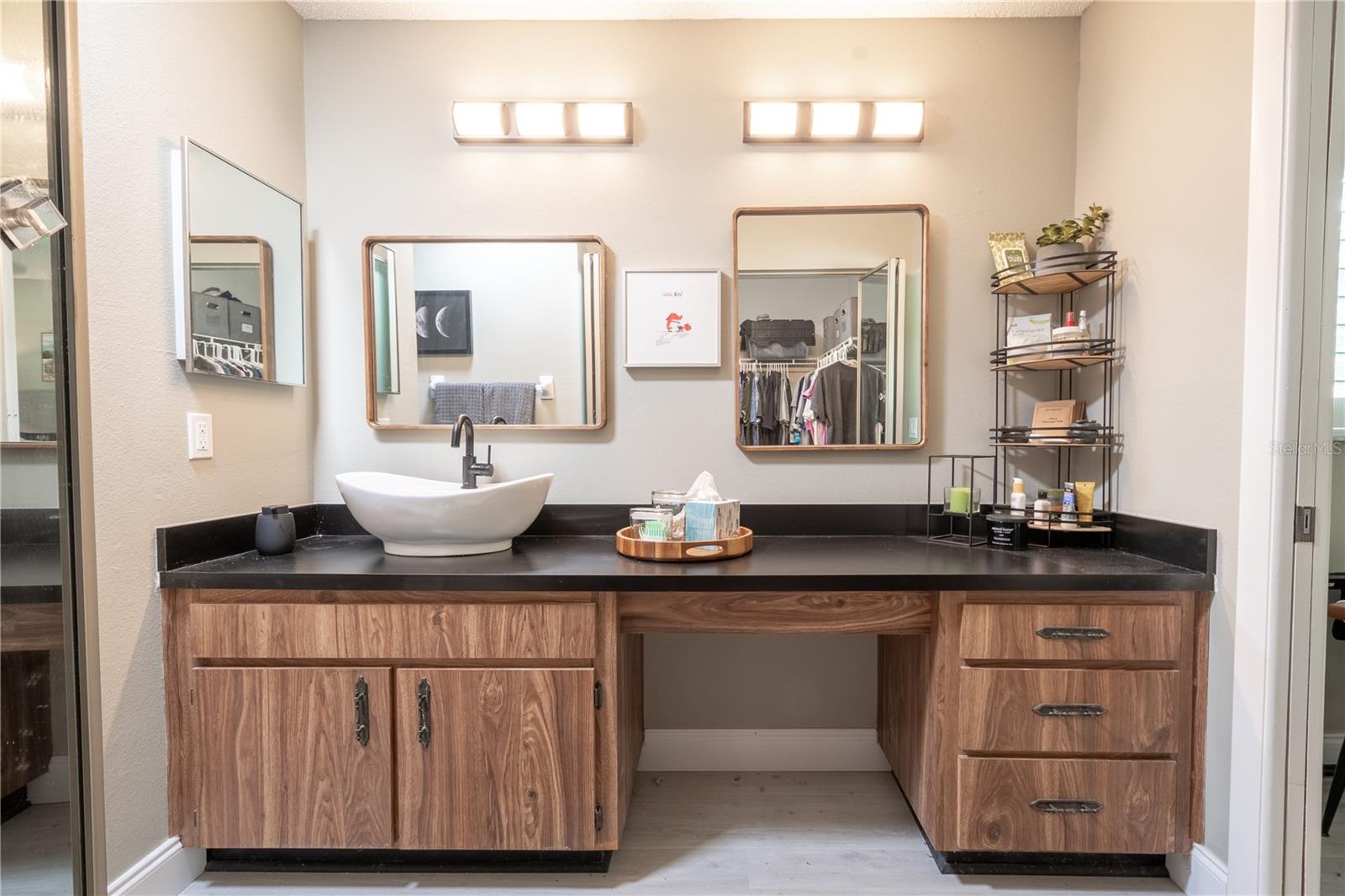 The primary ensuite bath features a mirrored vanity with vessel sink, storage and dual light fixtures.