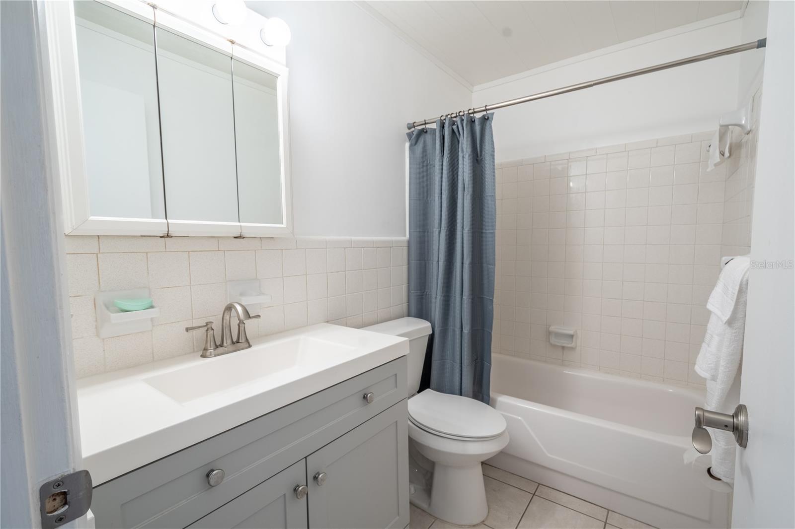 The bathroom features a mirrored vanity with storage, a tiled tub with shower and a ceramic tile floor, all done in neutral tones.