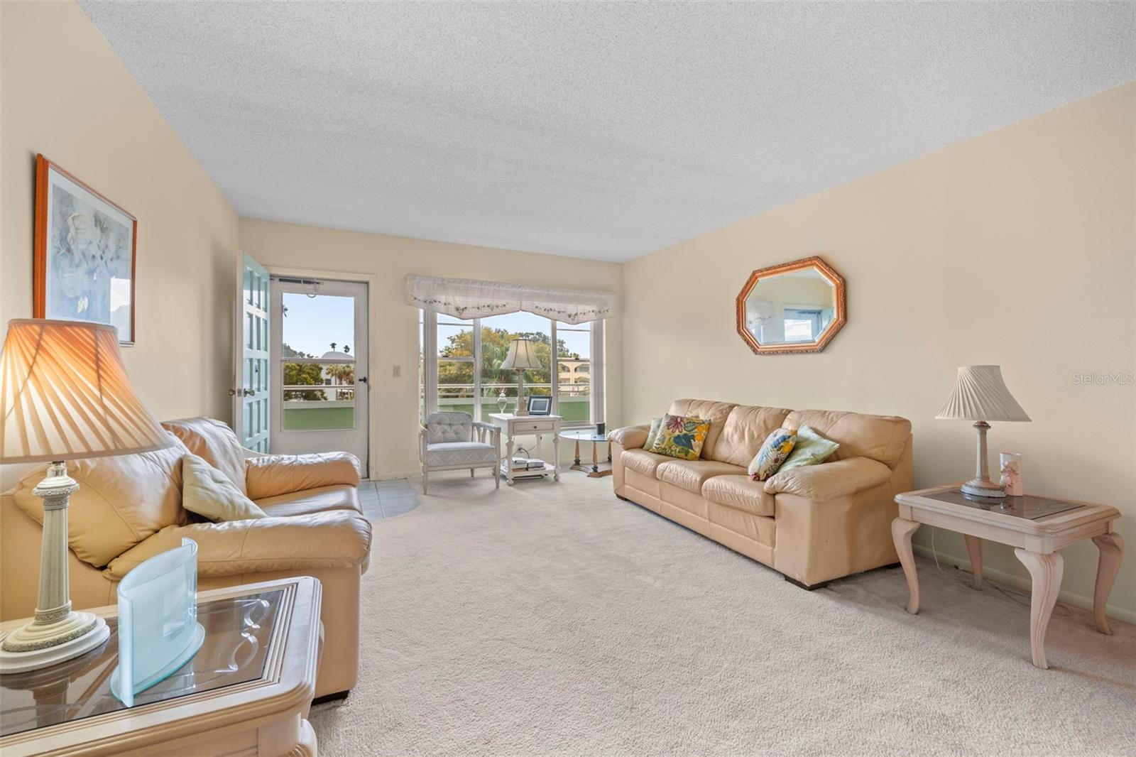 Light and bright view of the living room features a large picture window, storm door and neutral tones.