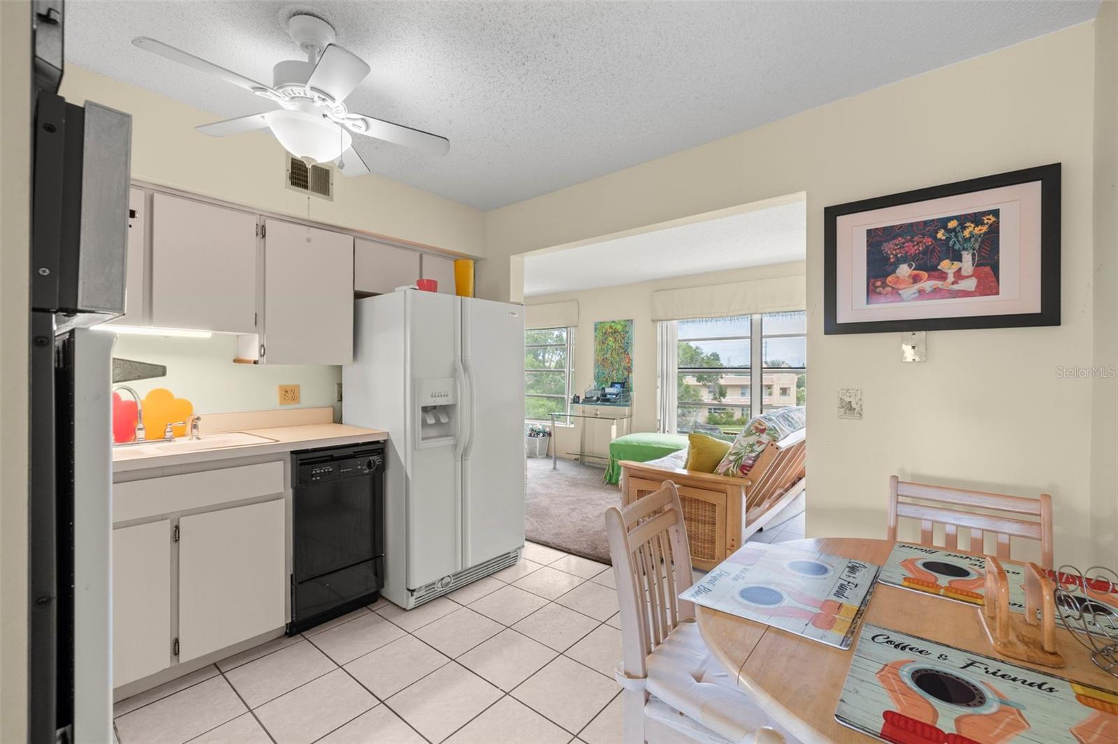 Eat-in bright kitchen with white cabinetry, ceramic flooring and ceiling fan. The kitchen is open to the flex-space/Florida room.