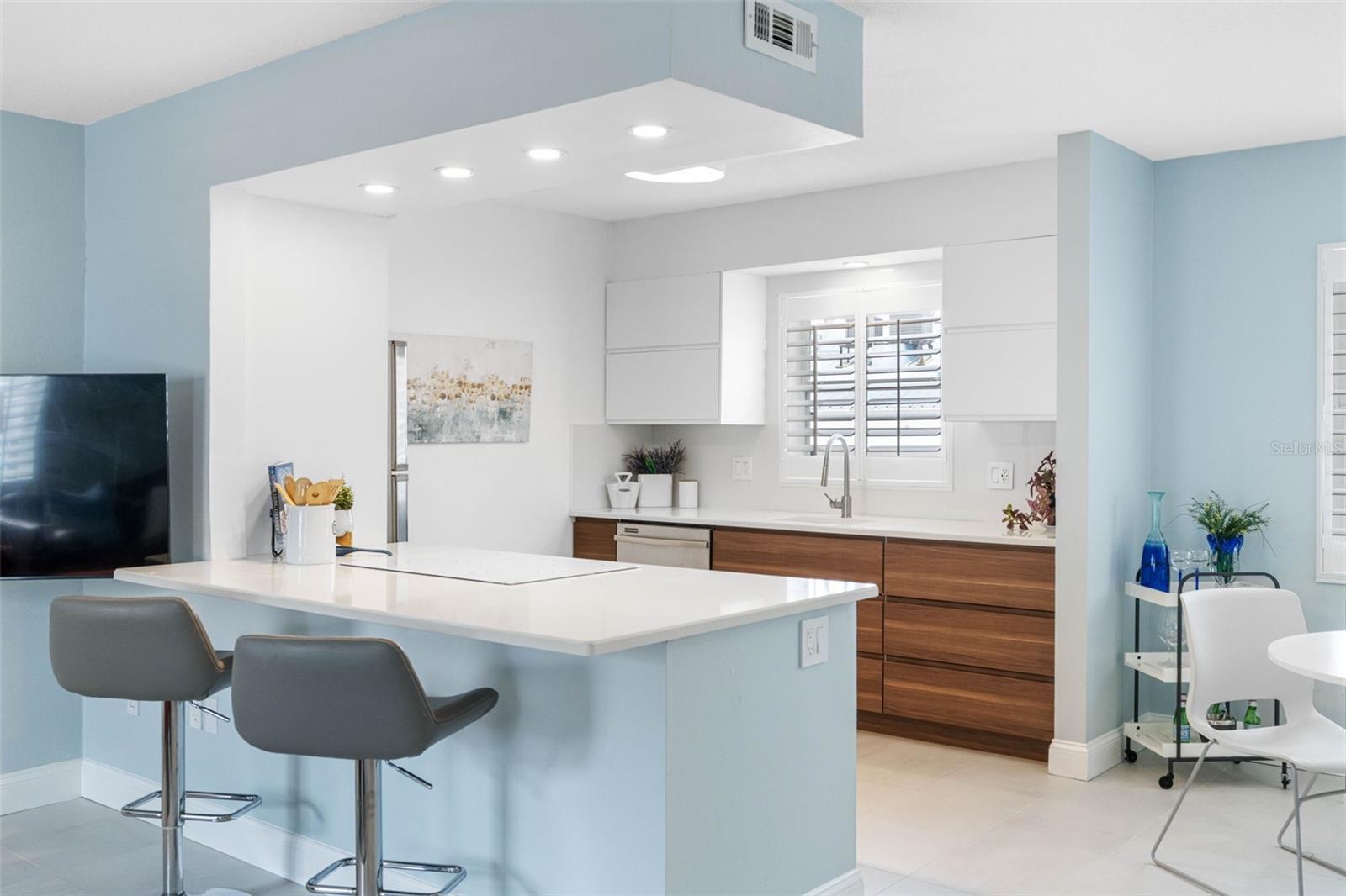 The kitchen features white cabinetry and stainless steel appliances, maintaining the clean and contemporary vibe.