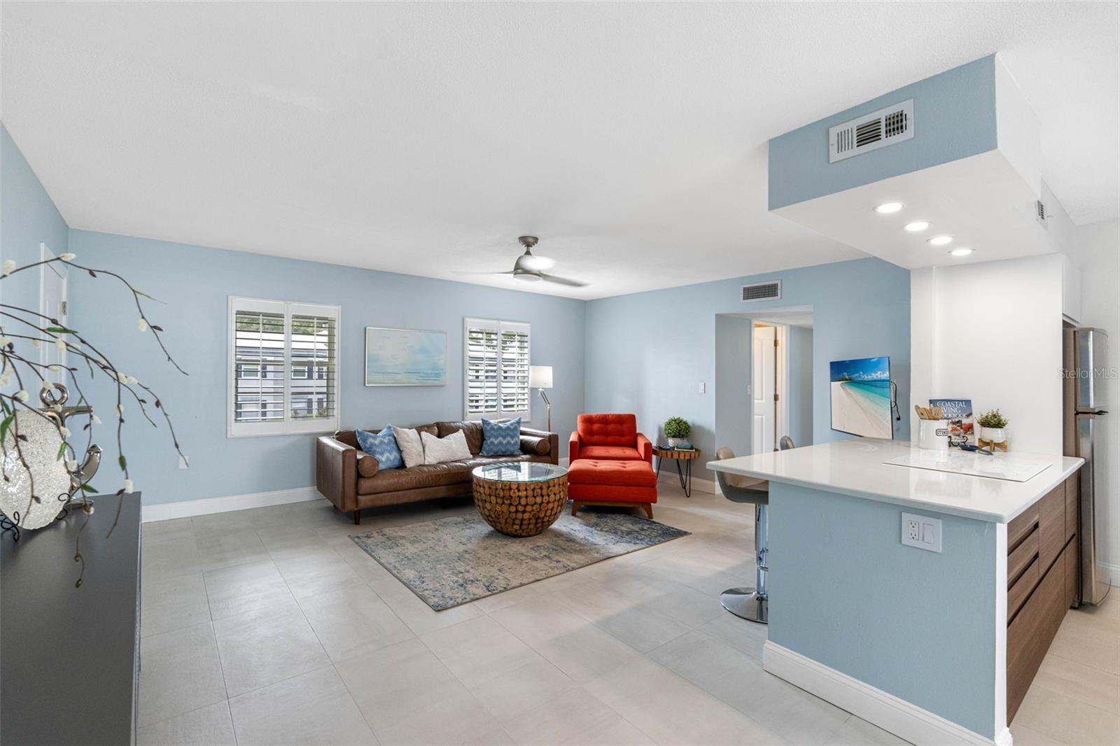 The room is painted in a soft, light blue that enhances its open and airy feel, complemented by a high ceiling with a modern ceiling fan that circulates air efficiently throughout the space,