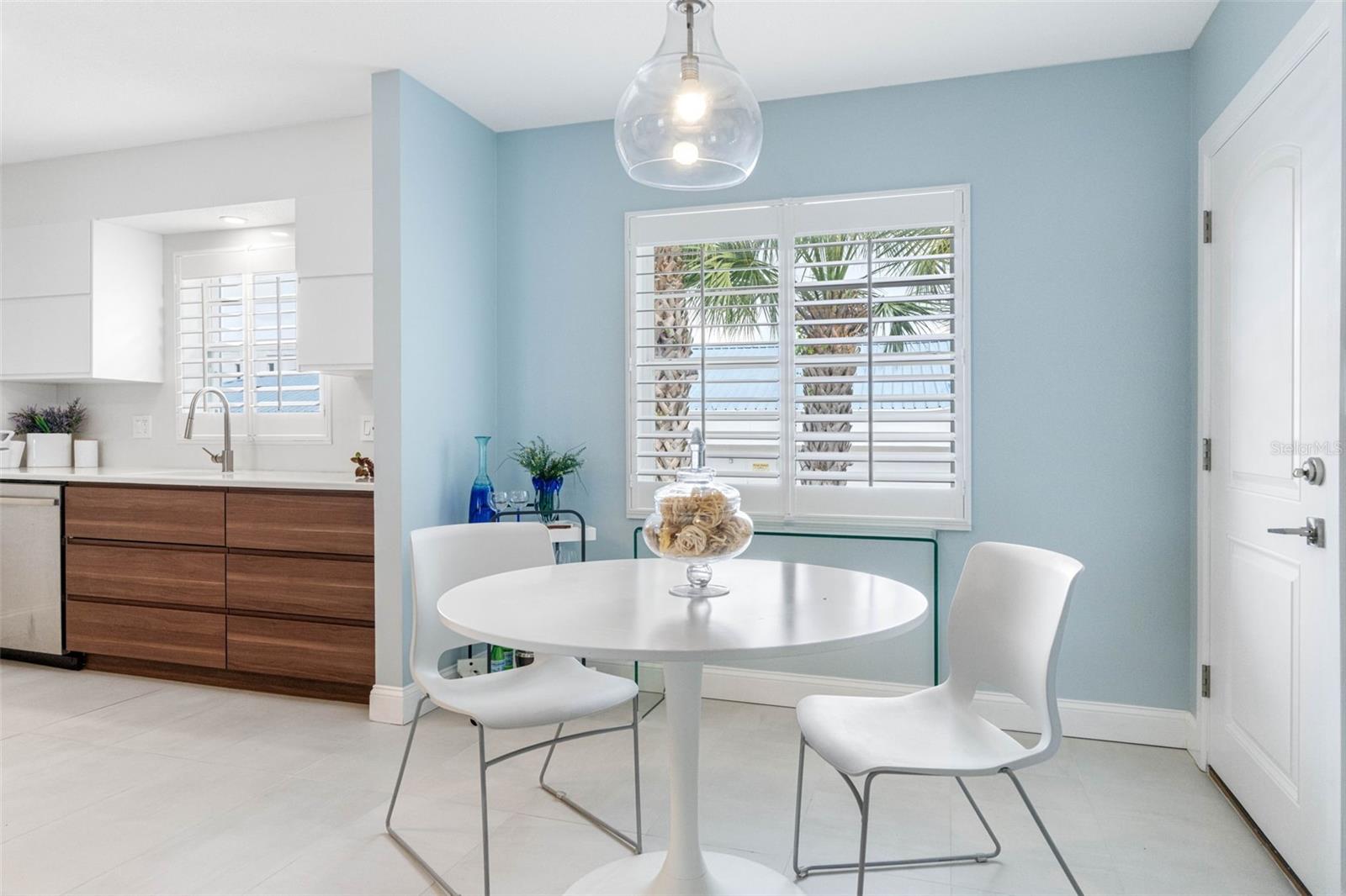 A small dining area with a round table and white chairs provides additional seating and a casual eating spot, illuminated by a chic pendant light.