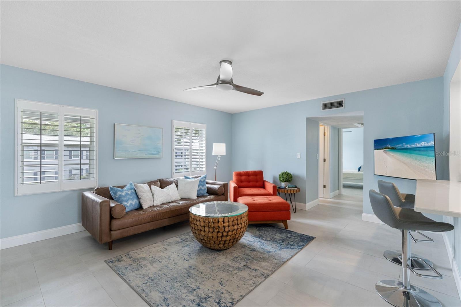 A large, plush leather sofa in a neutral tone offers ample seating, paired with vibrant orange accent chairs that add a pop of color and a lively contrast to the calm backdrop. Fully furnished.