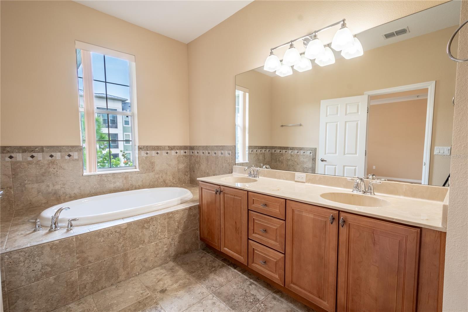 The primary ensuite bathroom features a dual sink, mirrored vanity with storage and downlight fixture, a garden tub and stylish ceramic tile.