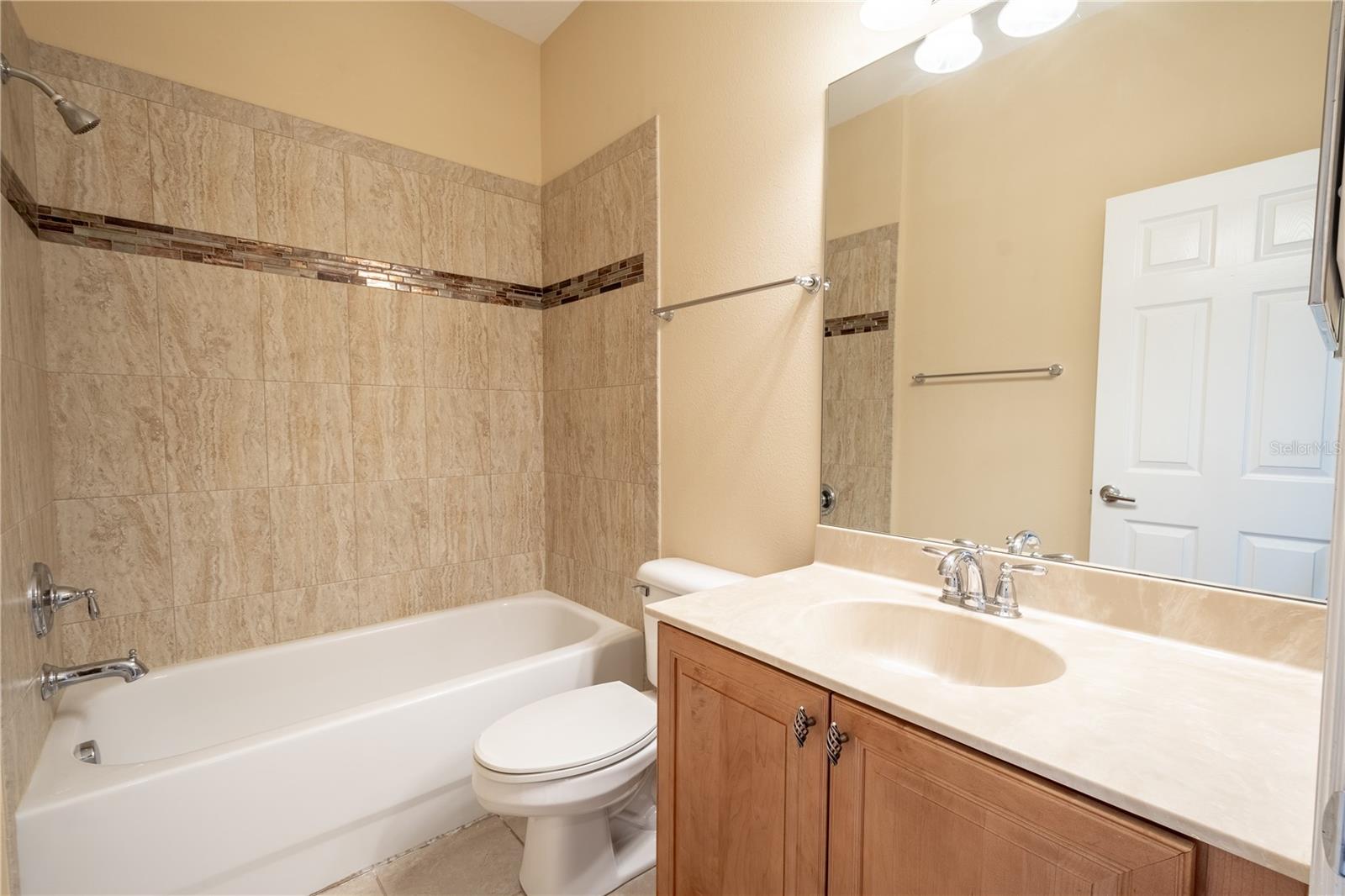 The upstairs full bath features a tiled tub with shower, a ceramic tile floor and a mirrored vanity with storage.