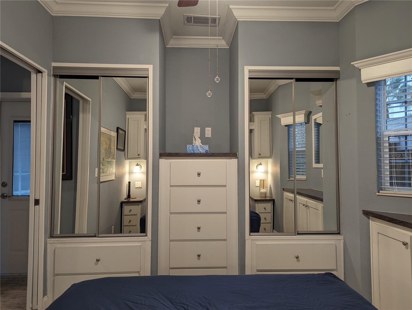 Built in drawers in the bedroom, ceiling fan, and sconce lights on both sides of bed.