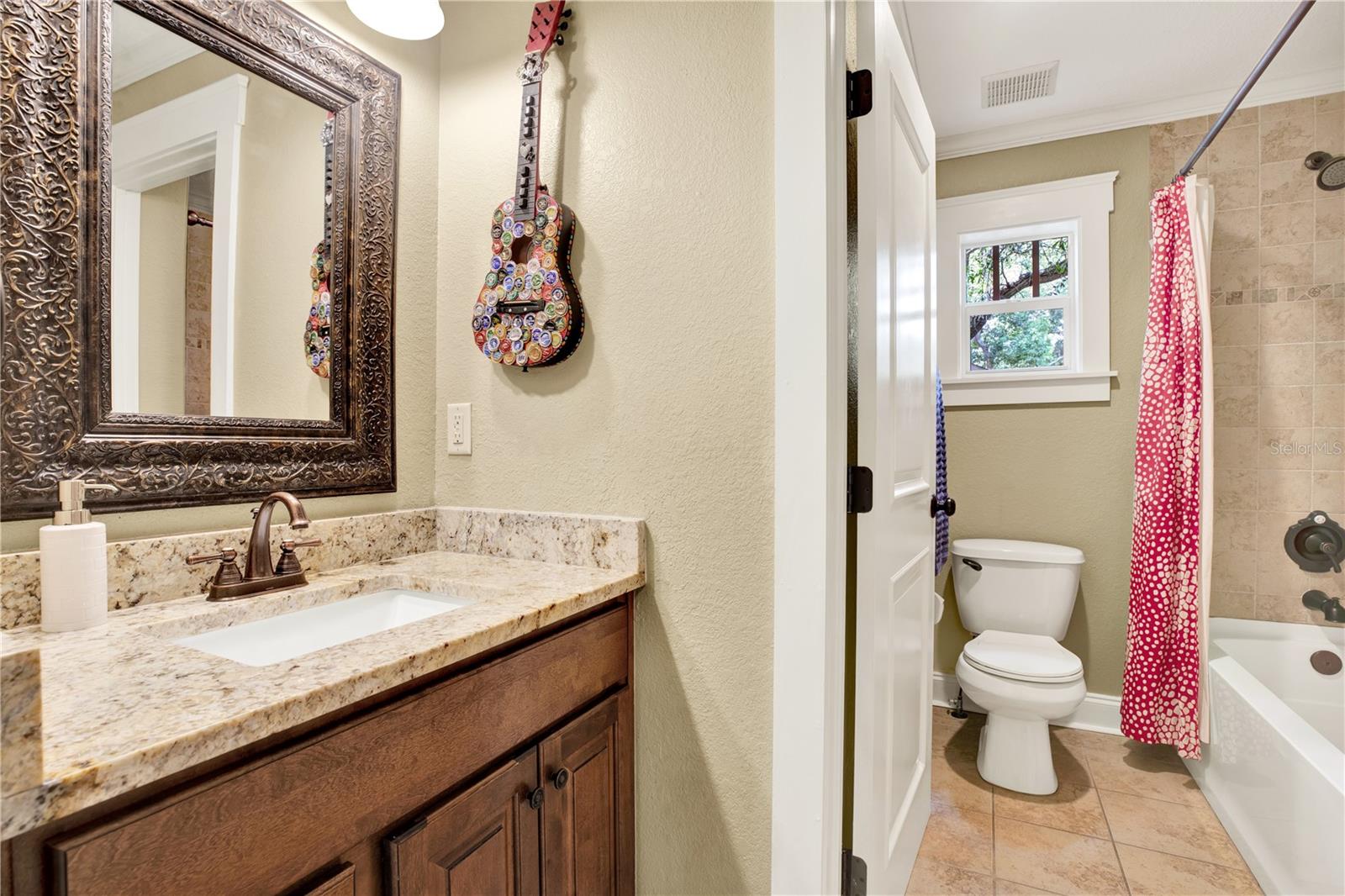 A second full bath upstairs features a bathtub/ shower combo and the same warm wood cabinetry and stone countertops