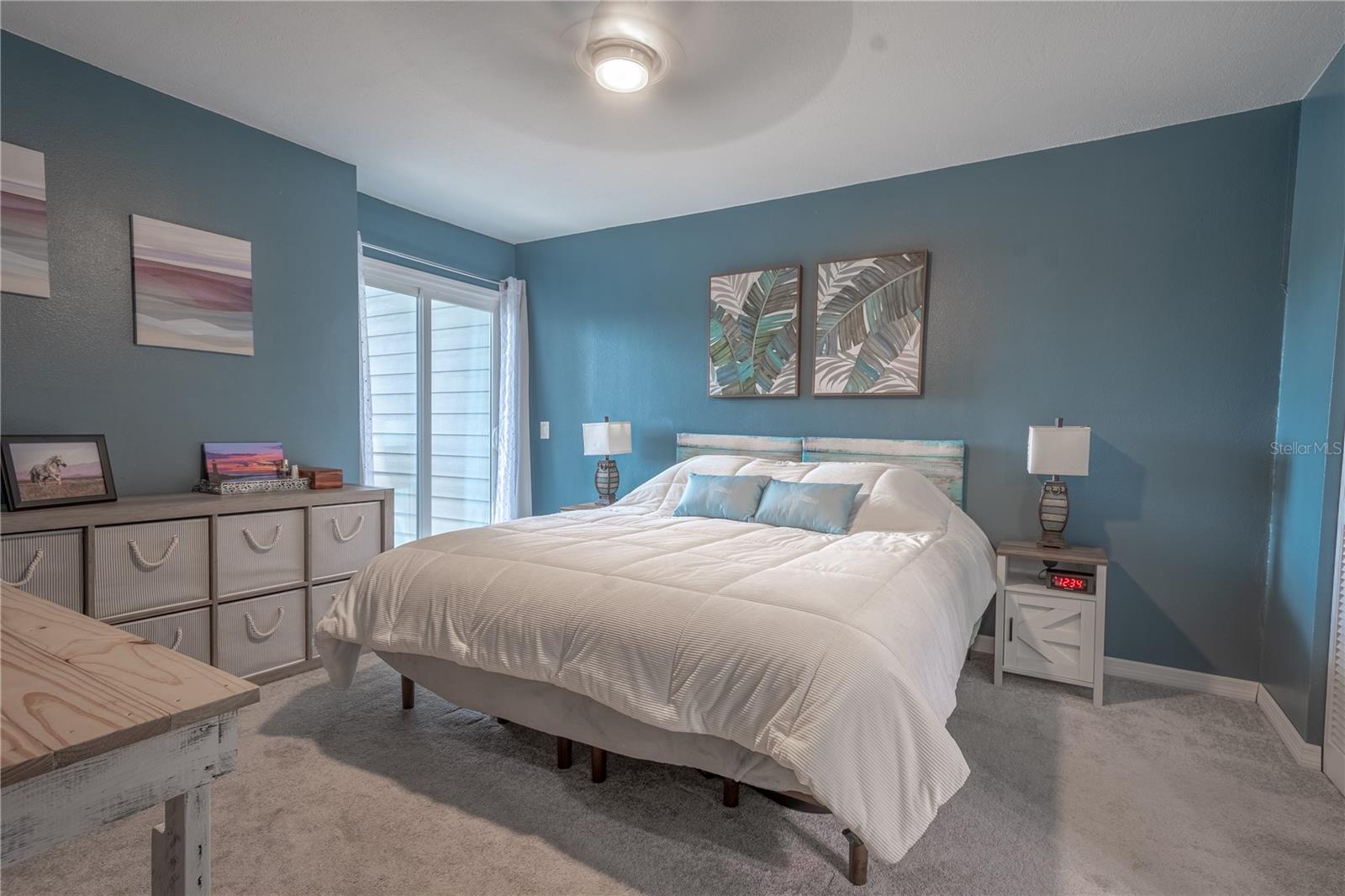 The primary bedroom features neutral tone carpet, an 8 blade ceiling fan with light kit for year round comfort and sliding glass doors to a private balcony with water view.