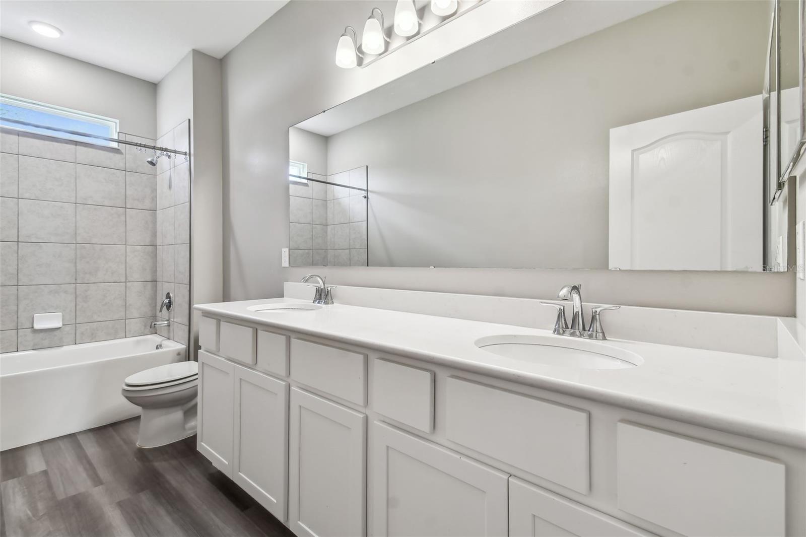 Second bath shared by second and third bedrooms. Extra long quartz counter. Double vanity. Designer light fixtures. Tub/shower combo with decorator tile.