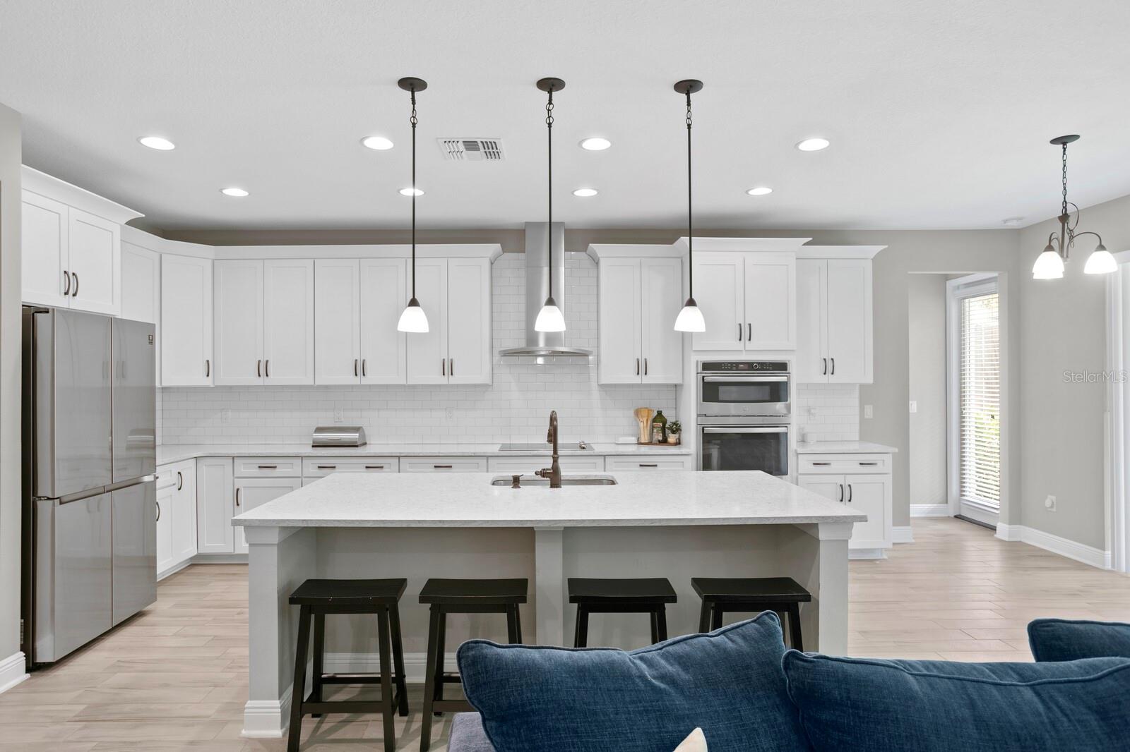 Kitchen has quartz countertops, overhead lighting fixtures, stainless steel appliances, and seating at the island.