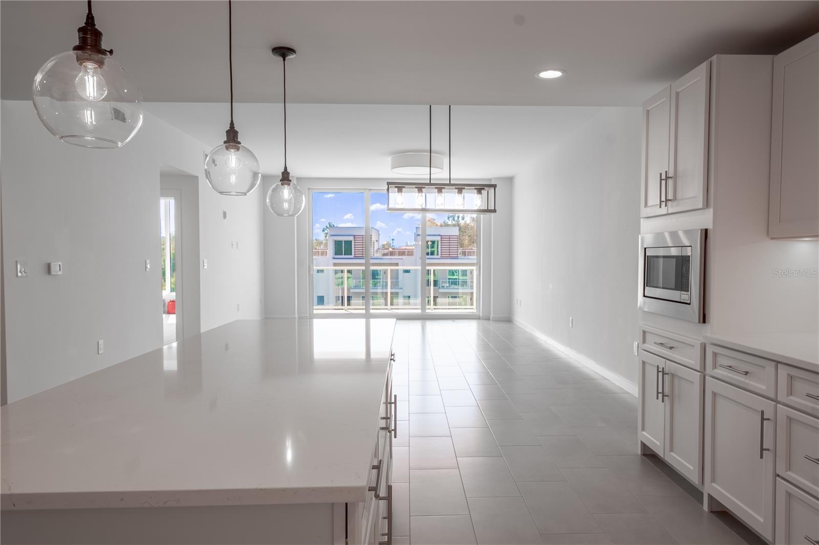 A linear candelabra bulb base at the center of the chandelier above your dining table casts a soft glow with a perfectly versatile look. The open floor plan is highlighted by a wall-to-wall sliding glass door that frames picturesque water views.