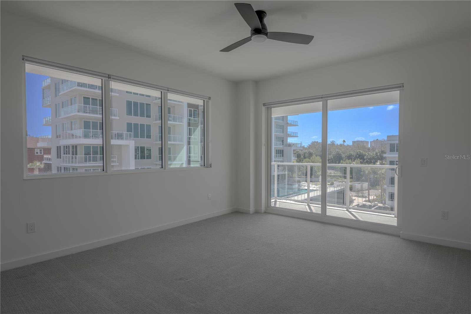 The carpeted primary bedroom is bathed in neutral tones with sliding glass doors to a private balcony.