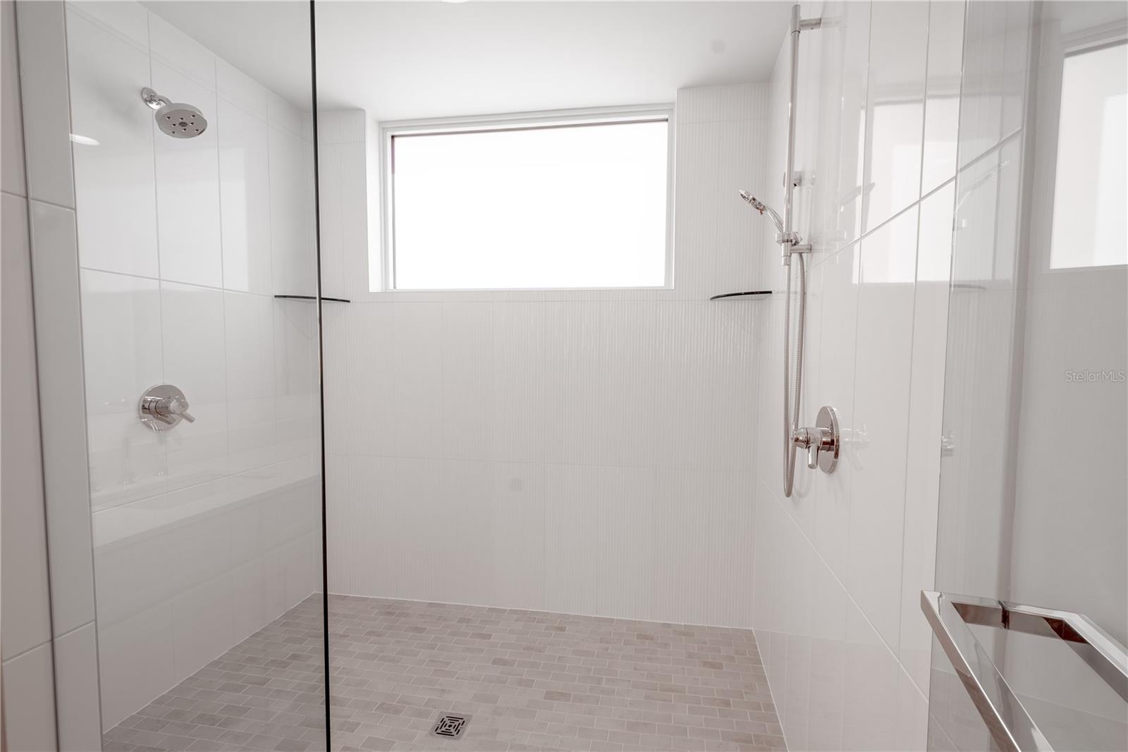 The primary bathroom oversized shower features multiple shower heads and a glass enclosure.