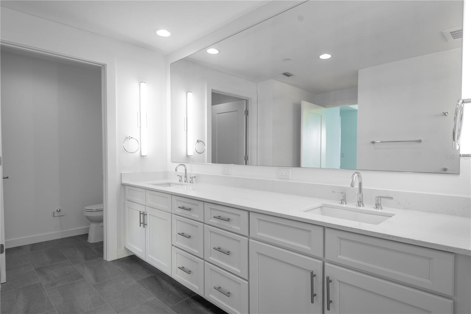 The primary bath features a private water closet and a dual sink, mirrored vanity with quartz countertop and storage, stylish wall sconces and recessed lighting.