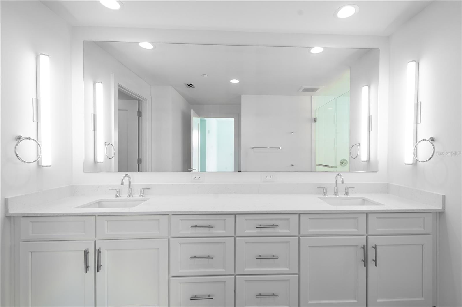 The primary bath features a dual sink, mirrored vanity with quartz countertop and storage, stylish wall sconces and recessed lighting.