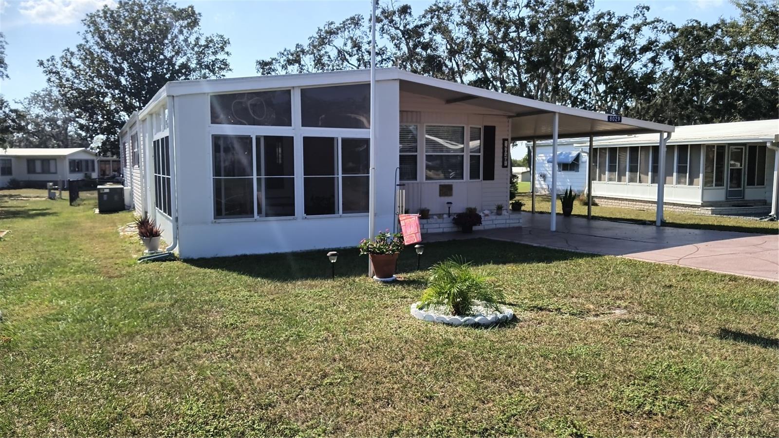 View of front depicts the large, vaulted ceiling front porch, front pay windows, carport and driveway.