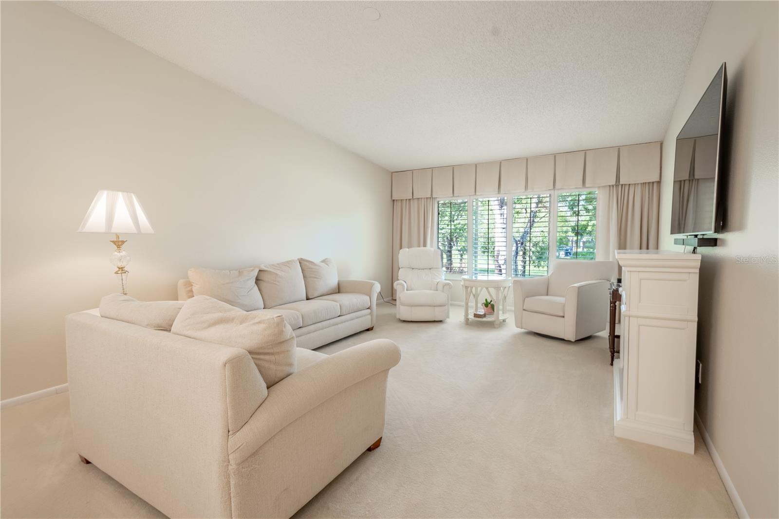 The living room is bathed in neutral tones, featuring custom drapery that frames the golf course view.