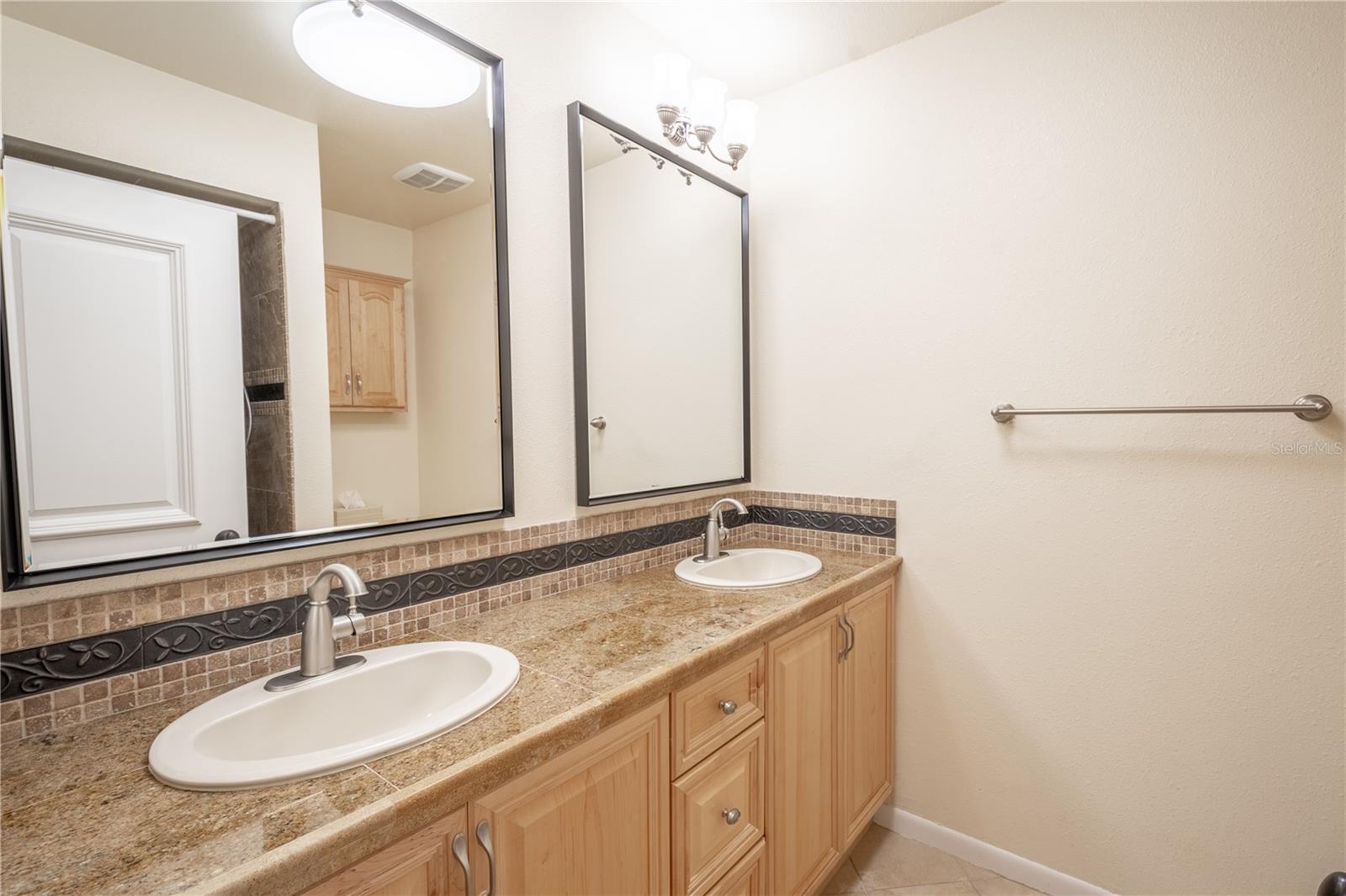 The primary ensuite bath features a mirrored dual sink vanity with storage, up light fixtures, granite counter tops with an artistic backspalsh.