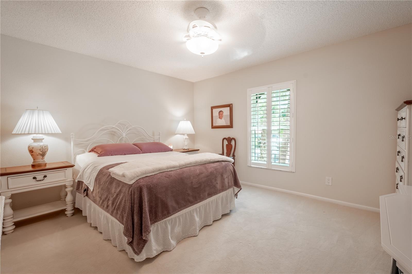 Bedroom two features the same inviting hues, plush carpet, a ceiling fan with light kit and plantation shutters.