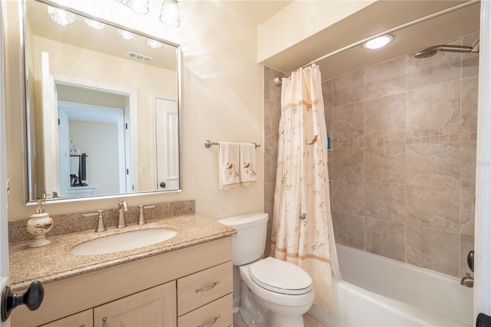 Bathroom two features a tiled tub with shower, ceramic tile floor, and a mirrored vanity with storage, granite couter and a down light fixture.