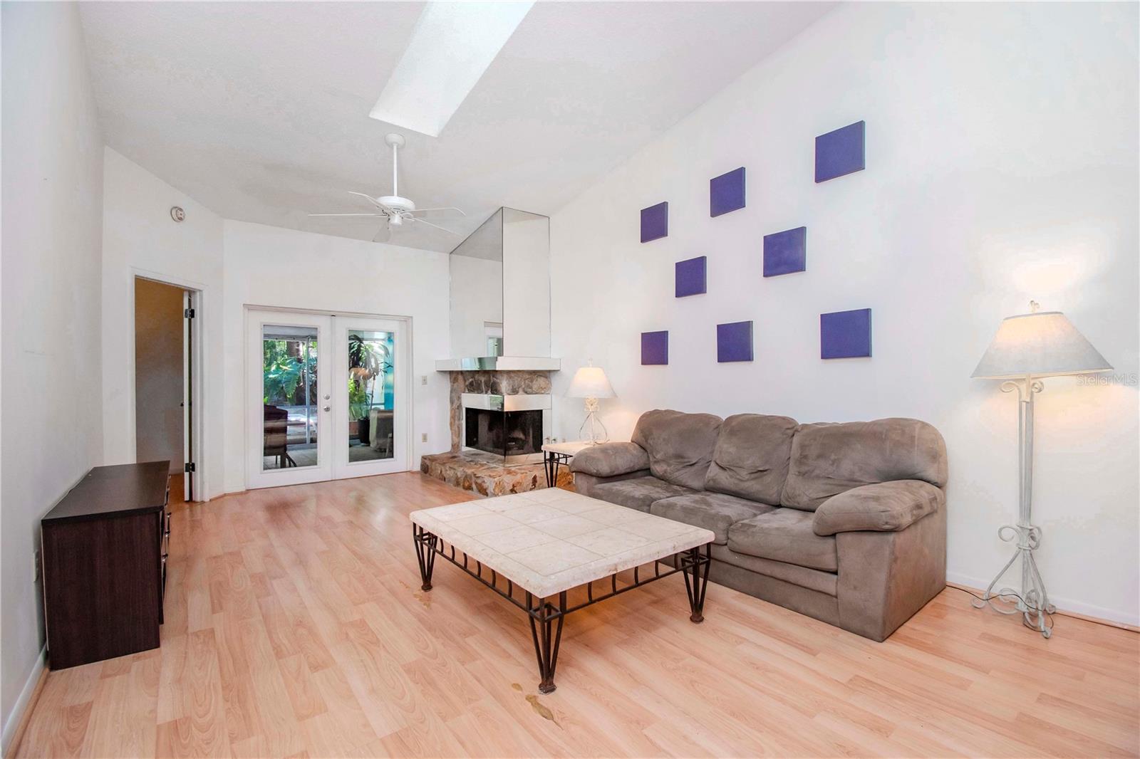 Living room area with the view into the primary bedroom, double doors to back enclosed porch and high ceilings with sky light.