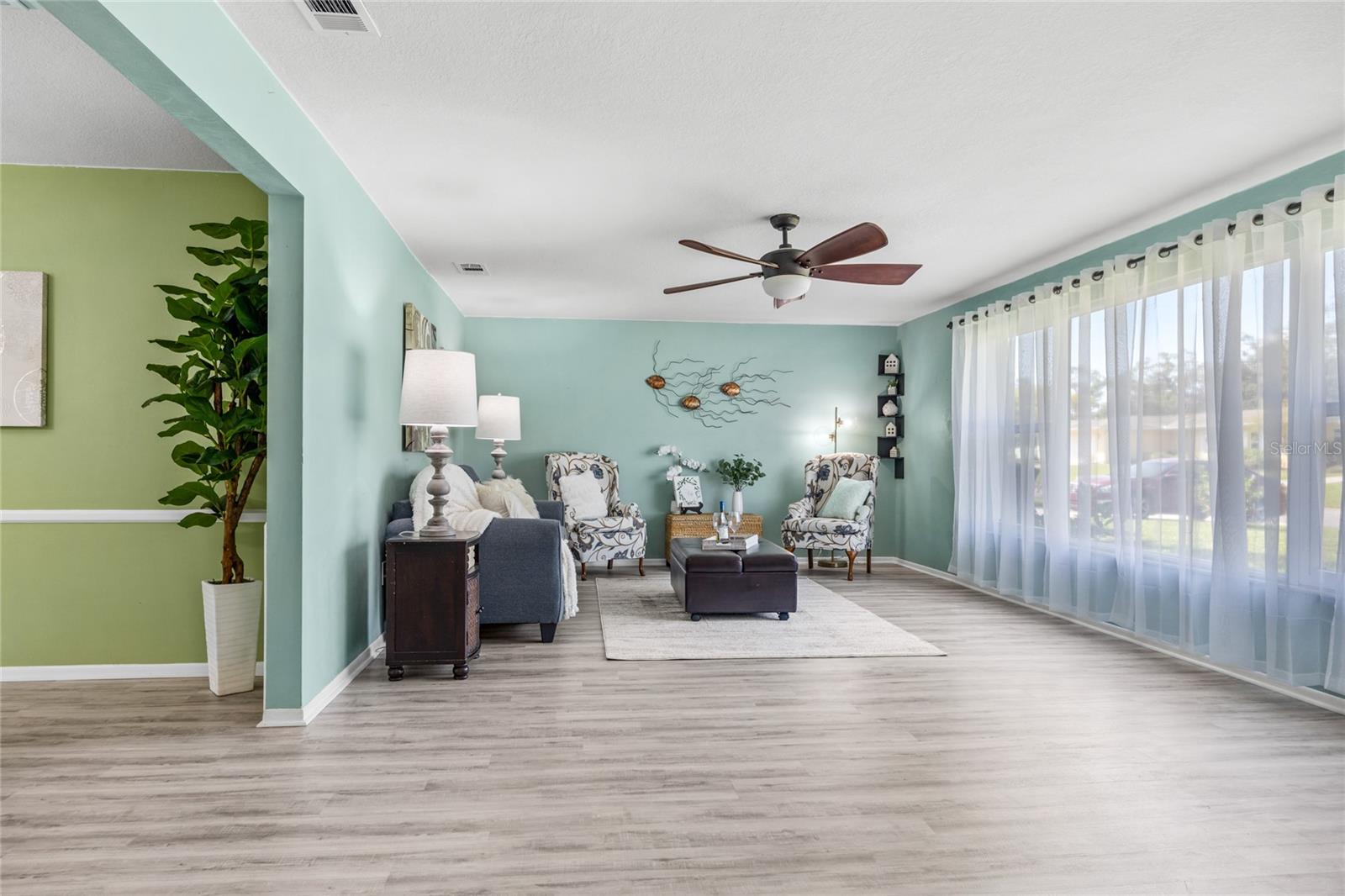 The formal Living Room offers an abundance of space, highlighted by luxurious vinyl flooring and oversized windows that bathe the room in natural light, while providing a picturesque view of the front yard.