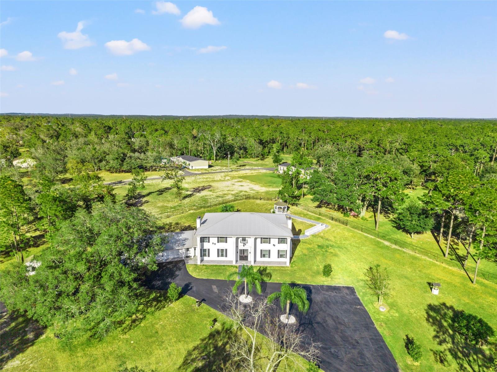 Aerial view of this Colonial-inspired estate, designed with the grandeur reminiscent of the iconic “White House.” Set on a private 2.40-acre property