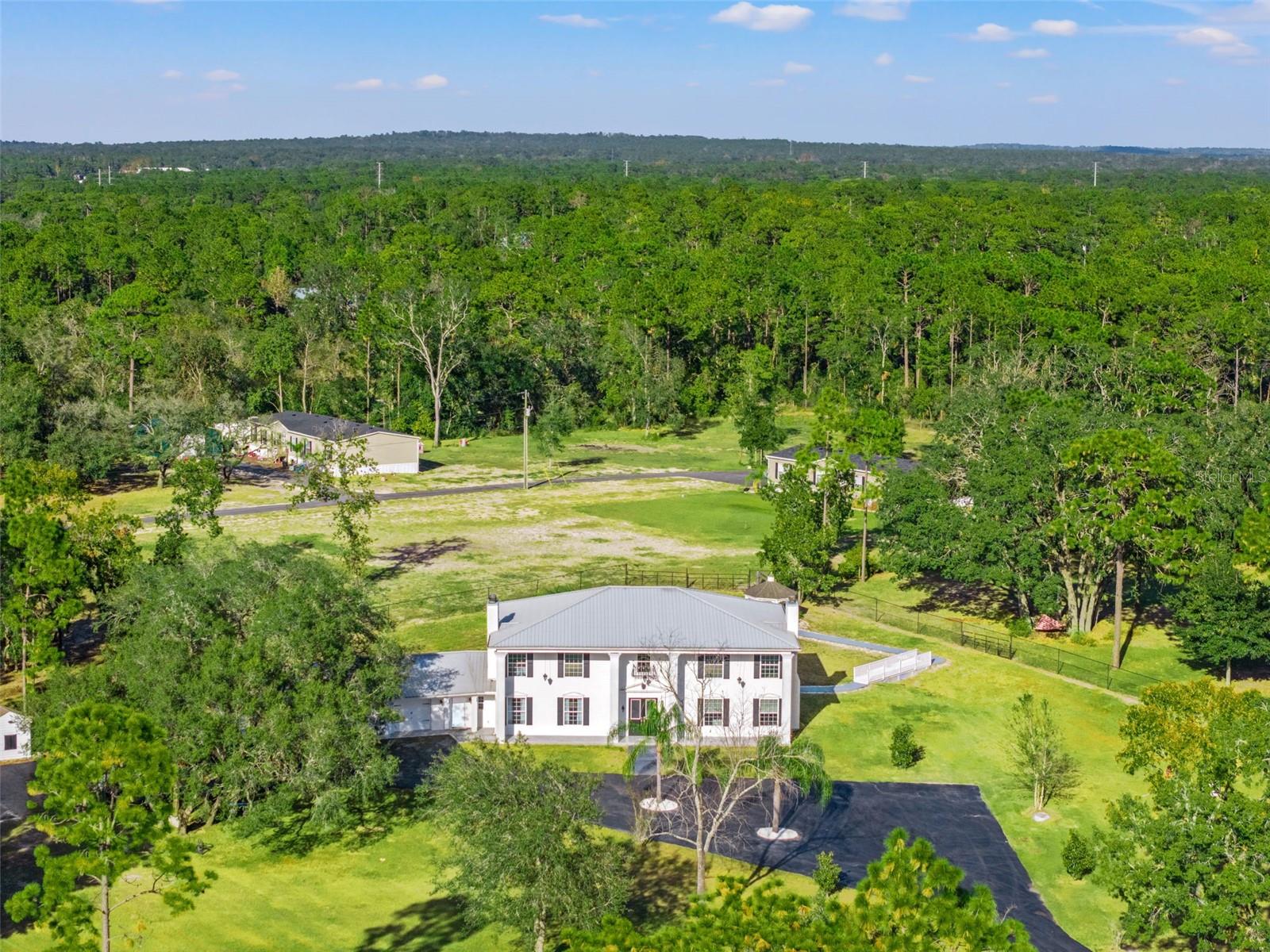 Aerial view of this Colonial-inspired estate, designed with the grandeur reminiscent of the iconic “White House.” Set on a private 2.40-acre property