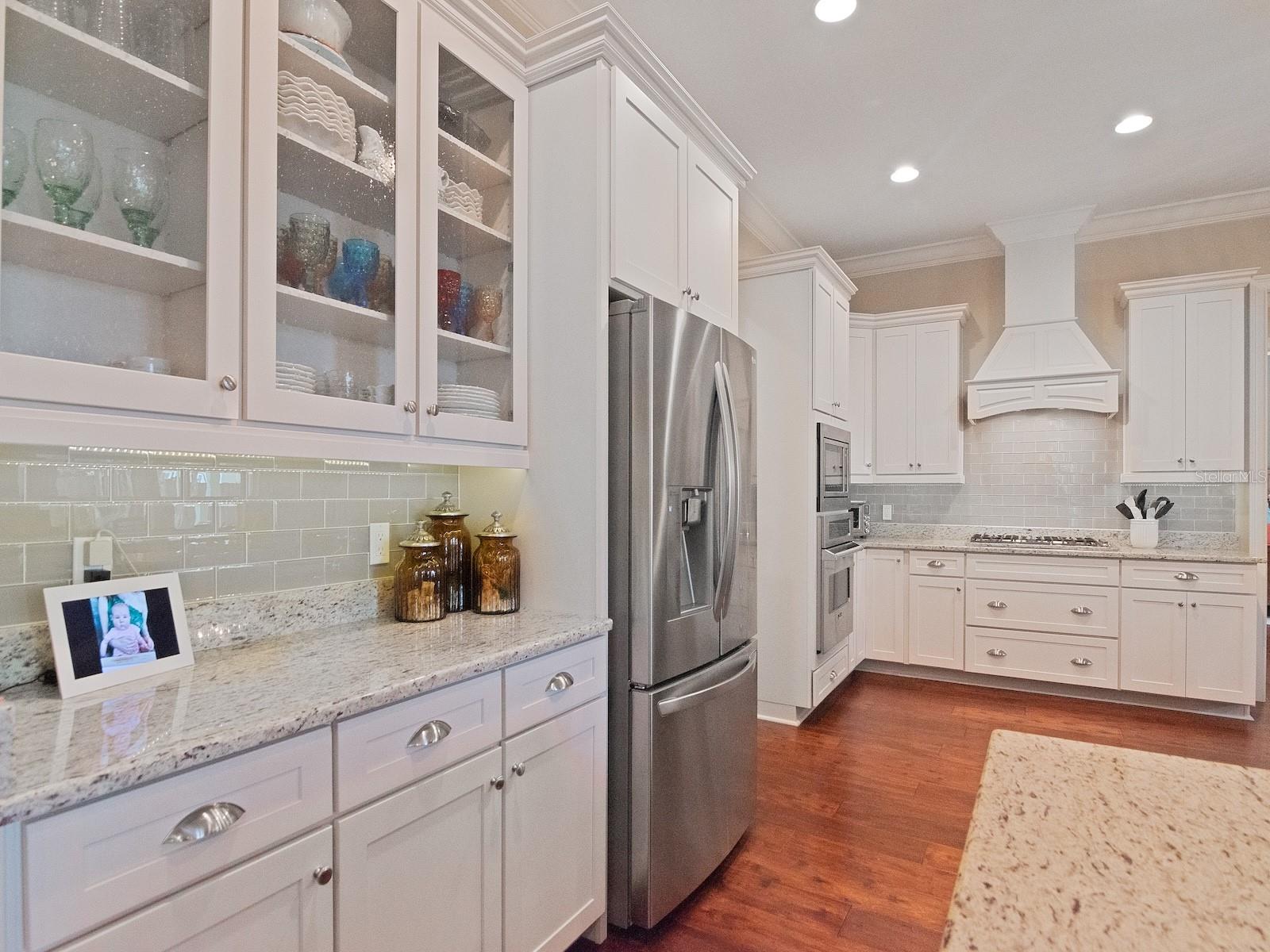 Glass upper cabinets, neutral tiled backsplash, and wood dressed exhaust fan reflect attention to detail